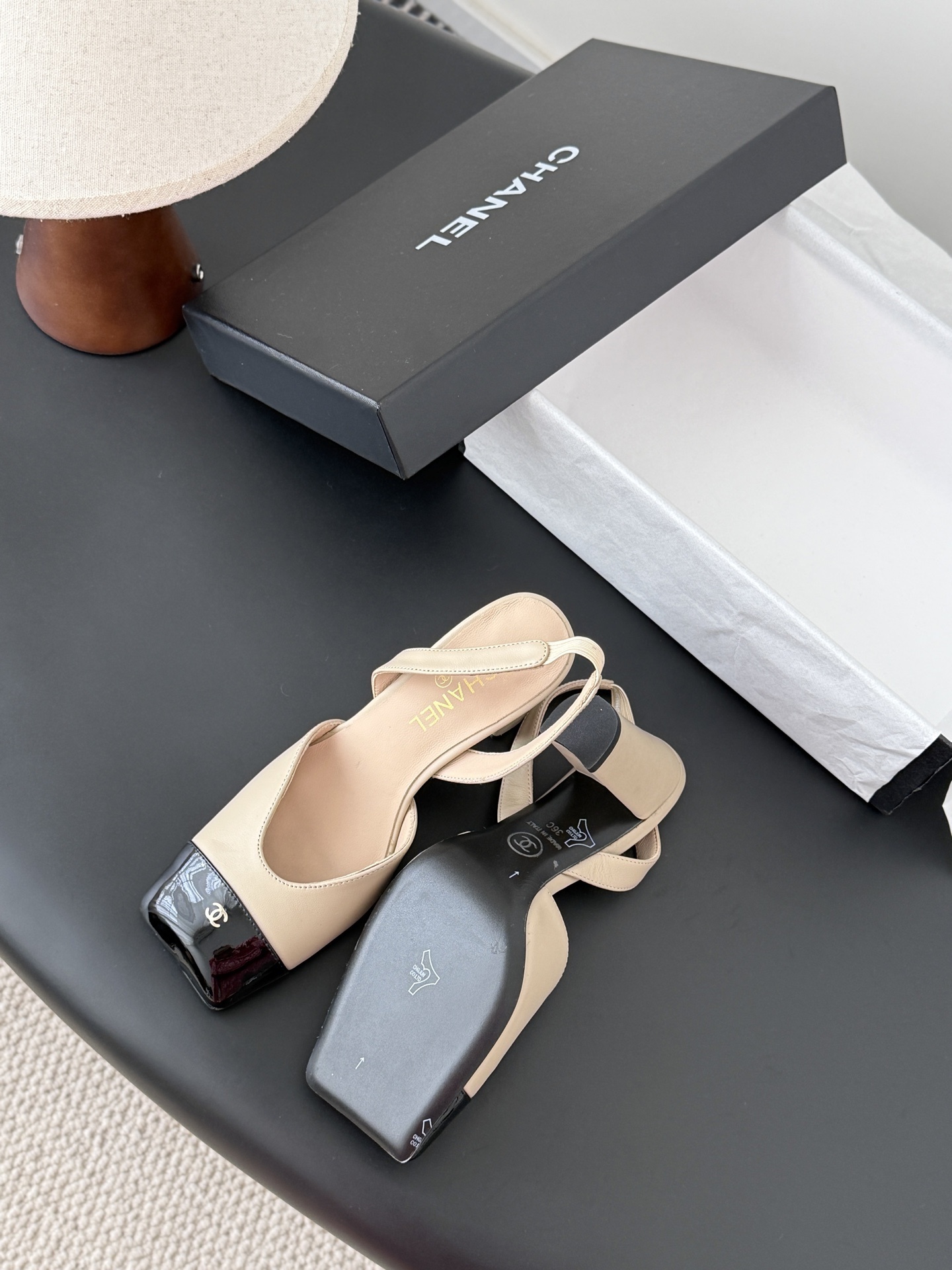 Pair of Chanel beige leather slingback pumps with black patent toe caps and block heels on a black table - Hình 5