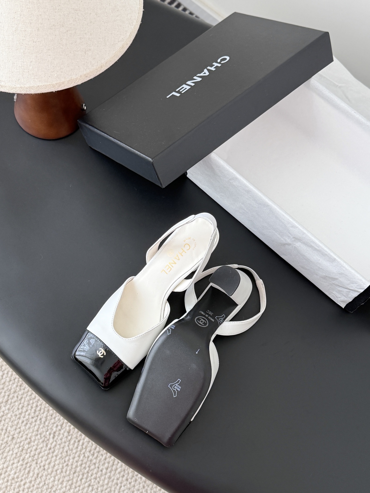 Luxury Chanel white leather slingback pumps with black patent cap toes and gold CC logo, displayed next to a Chanel shoe box. - Hình 5