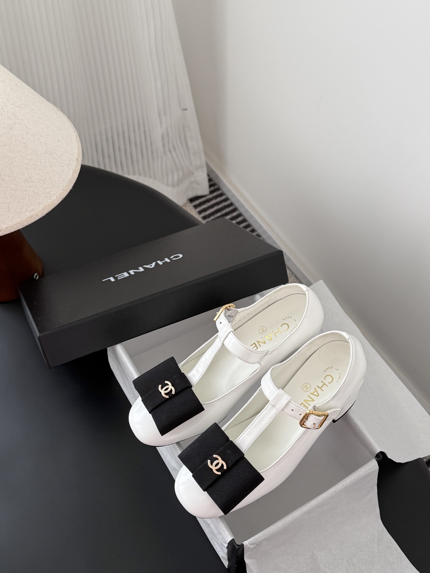 Chanel white patent leather Mary Jane block heels with black bows and gold CC logos shown with original packaging. - Hình 9