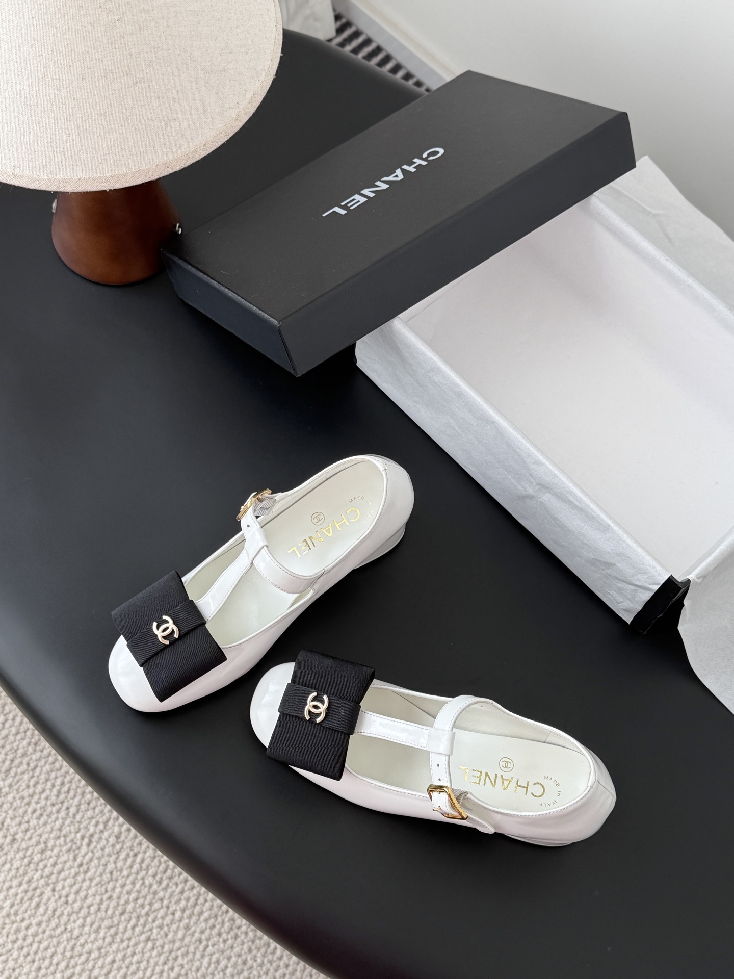 Chanel white patent leather Mary Jane block heels with black bows and gold CC logos shown with original packaging. - Hình 6