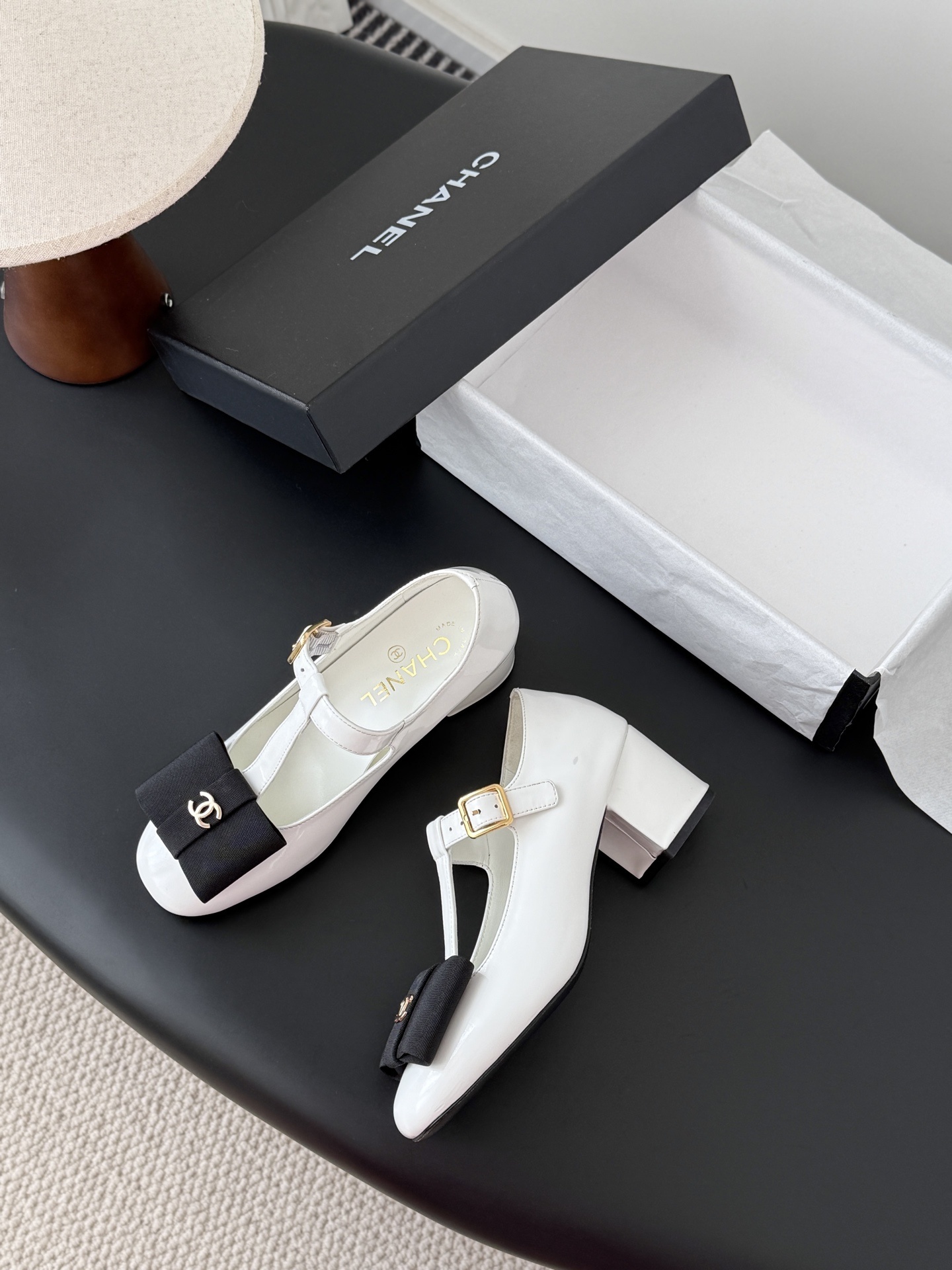 Chanel white patent leather Mary Jane block heels with black bows and gold CC logos shown with original packaging. - Hình 4