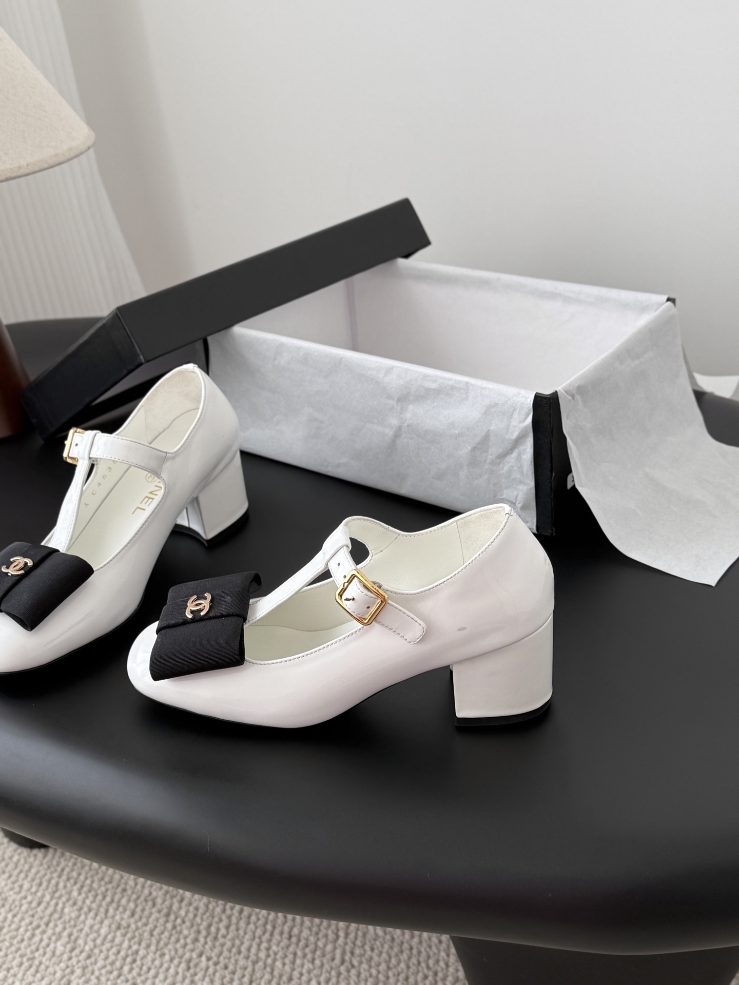 Chanel white patent leather Mary Jane block heels with black bows and gold CC logos shown with original packaging. - Hình 2
