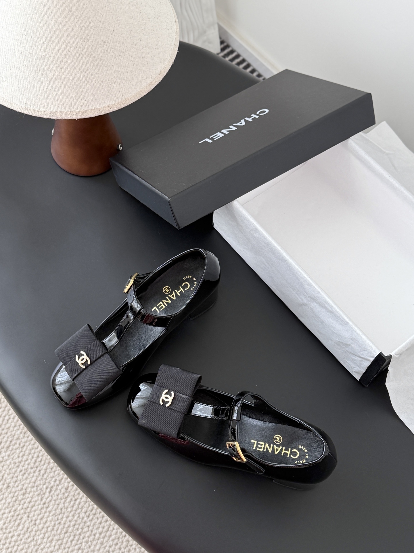Pair of black Chanel patent leather Mary Jane pumps with T-strap, gold CC logo bow, and block heel next to a Chanel shoe box. - Hình 6