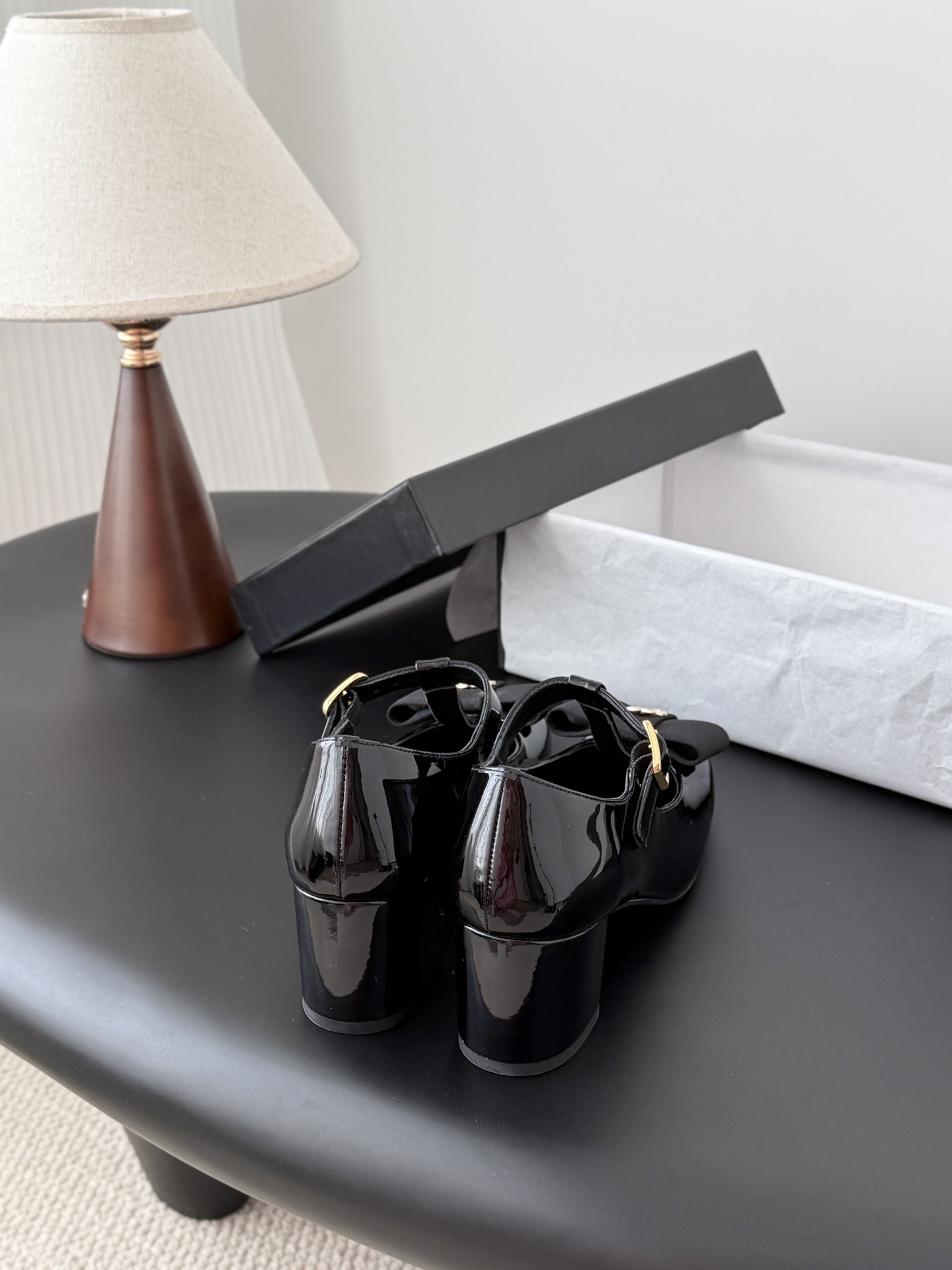 Pair of black Chanel patent leather Mary Jane pumps with T-strap, gold CC logo bow, and block heel next to a Chanel shoe box. - Hình 3