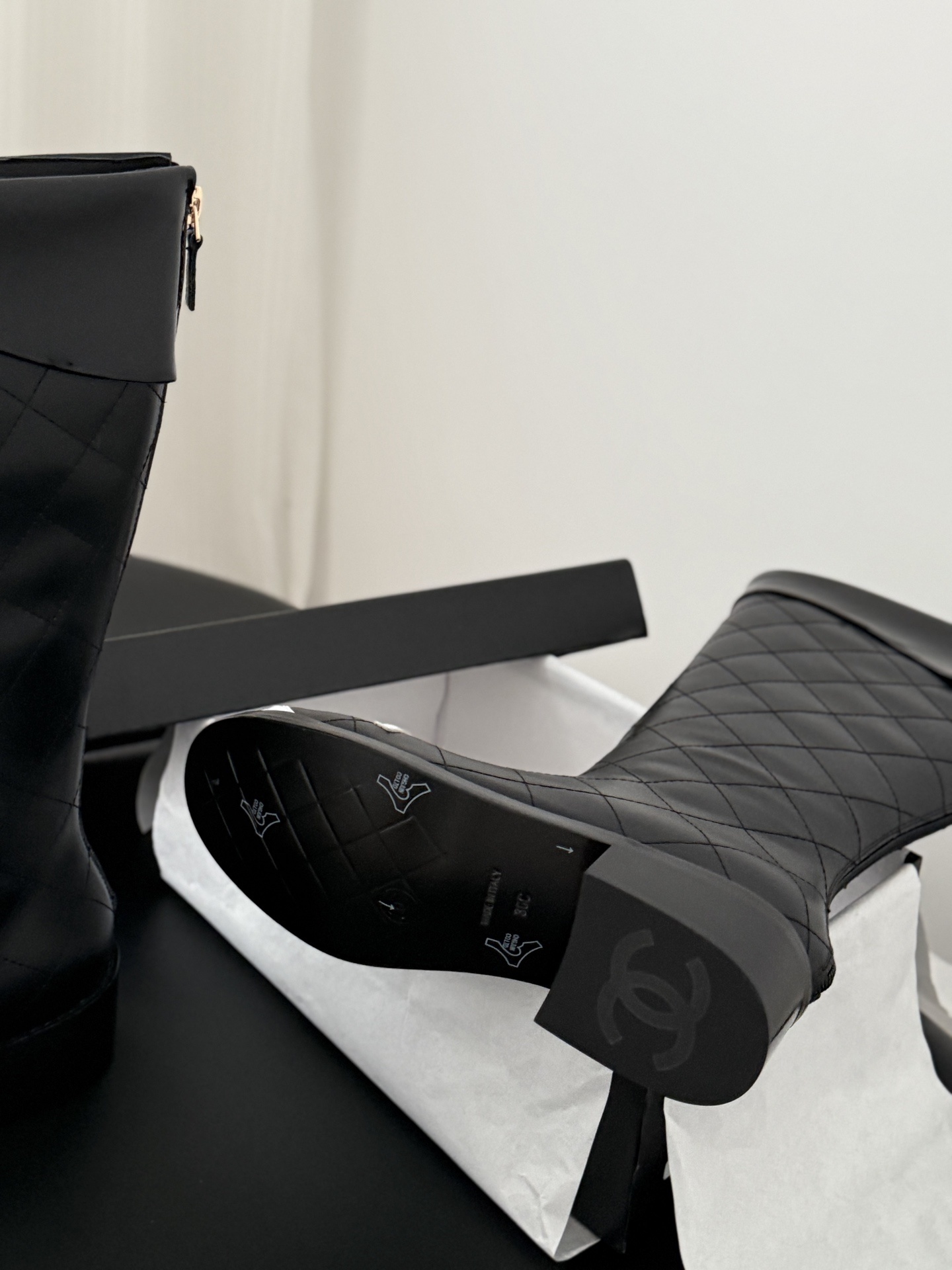 A pair of Chanel black quilted leather knee-high boots with white interlocking CC logos on the toe caps and gold-tone back zippers. - Hình 5