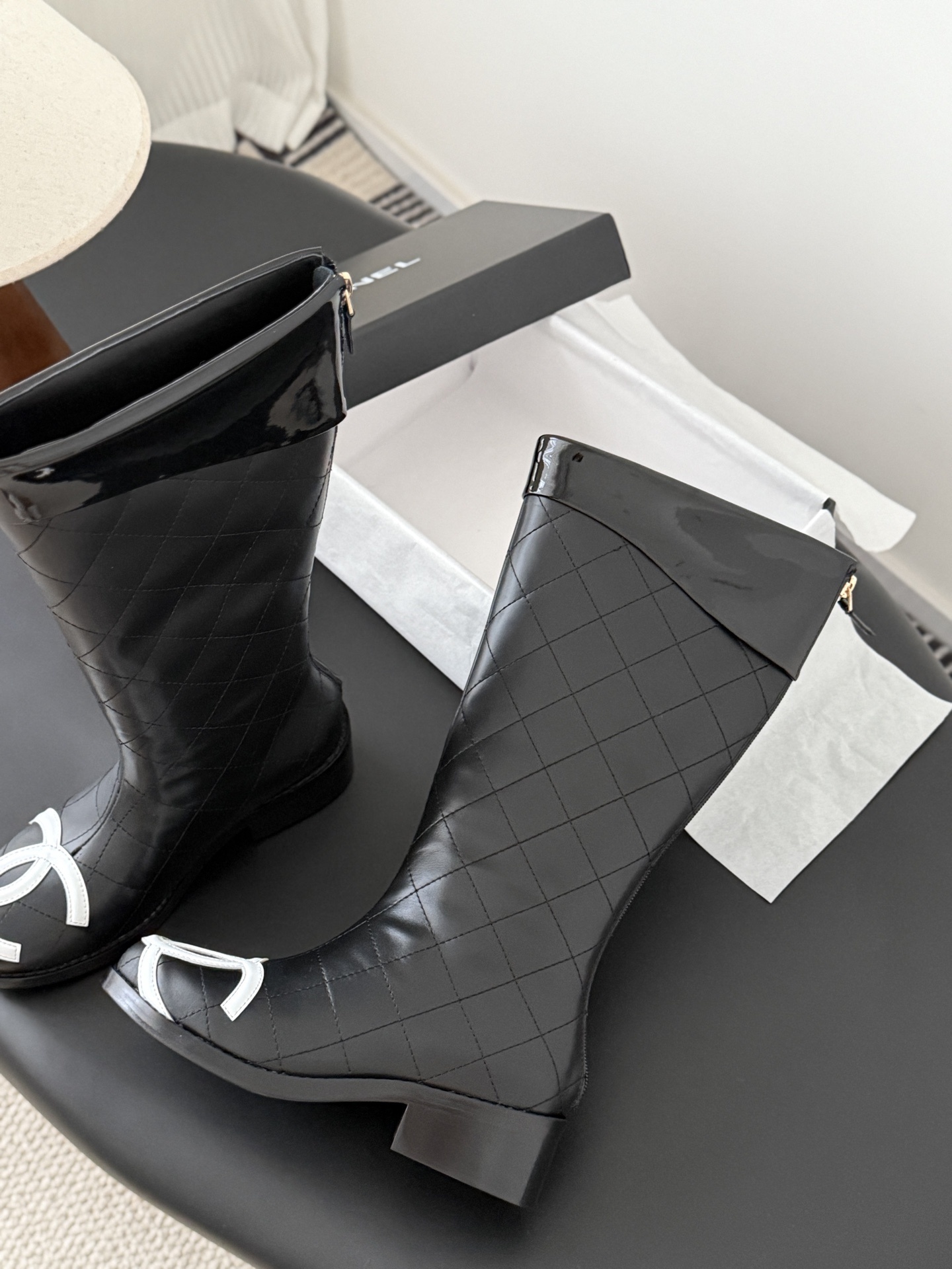 A pair of Chanel black quilted leather knee-high boots with white interlocking CC logos on the toe caps and gold-tone back zippers. - Hình 4