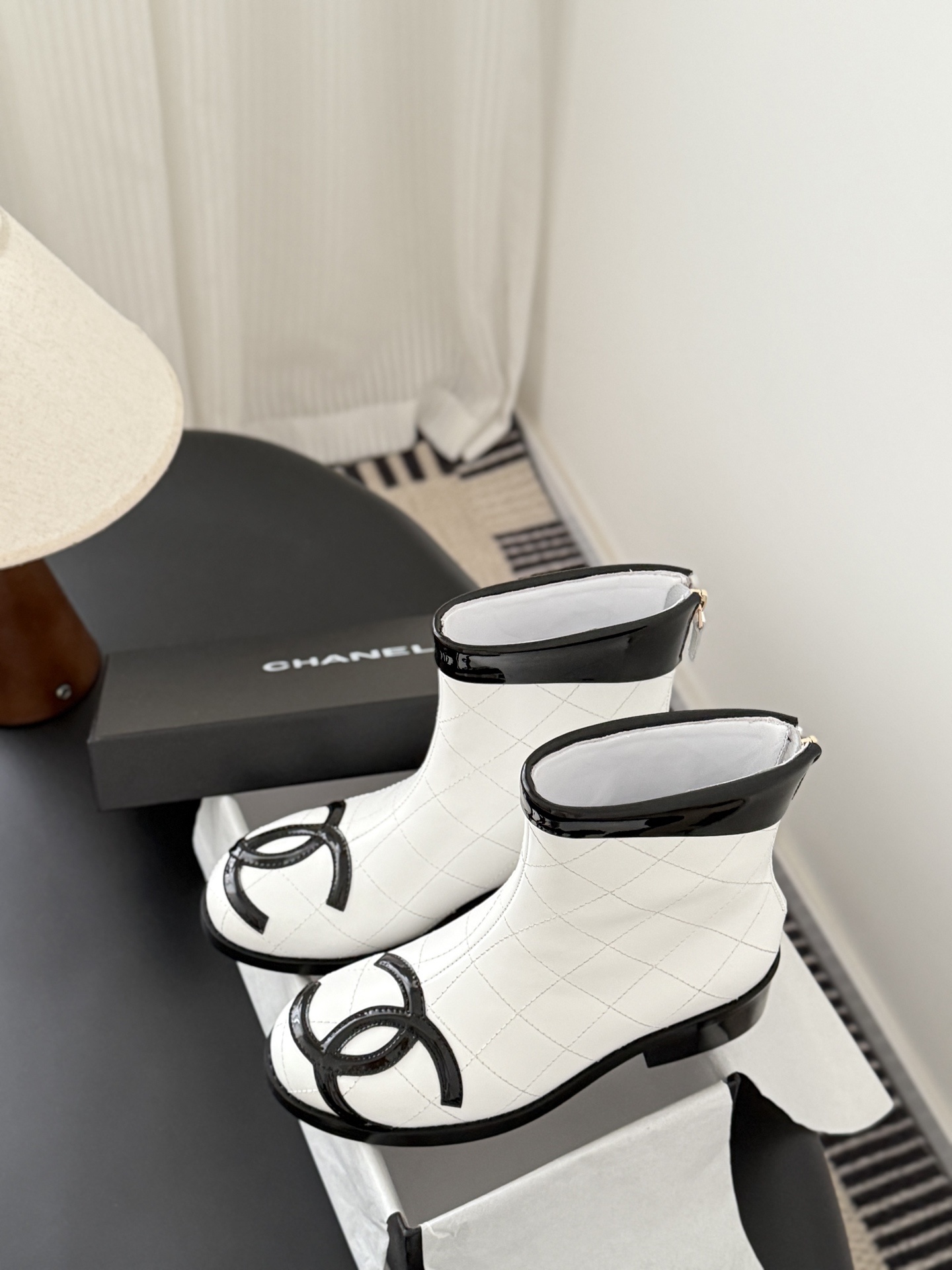 Pair of Chanel white quilted leather ankle boots with black patent leather toe caps and interlocking CC logos on a black surface. - Hình 9