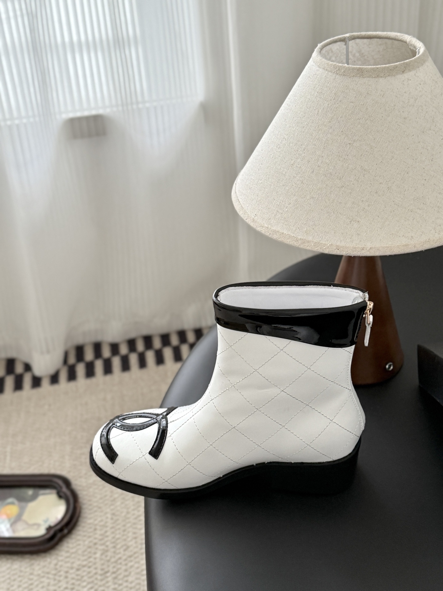 Pair of Chanel white quilted leather ankle boots with black patent leather toe caps and interlocking CC logos on a black surface. - Hình 8