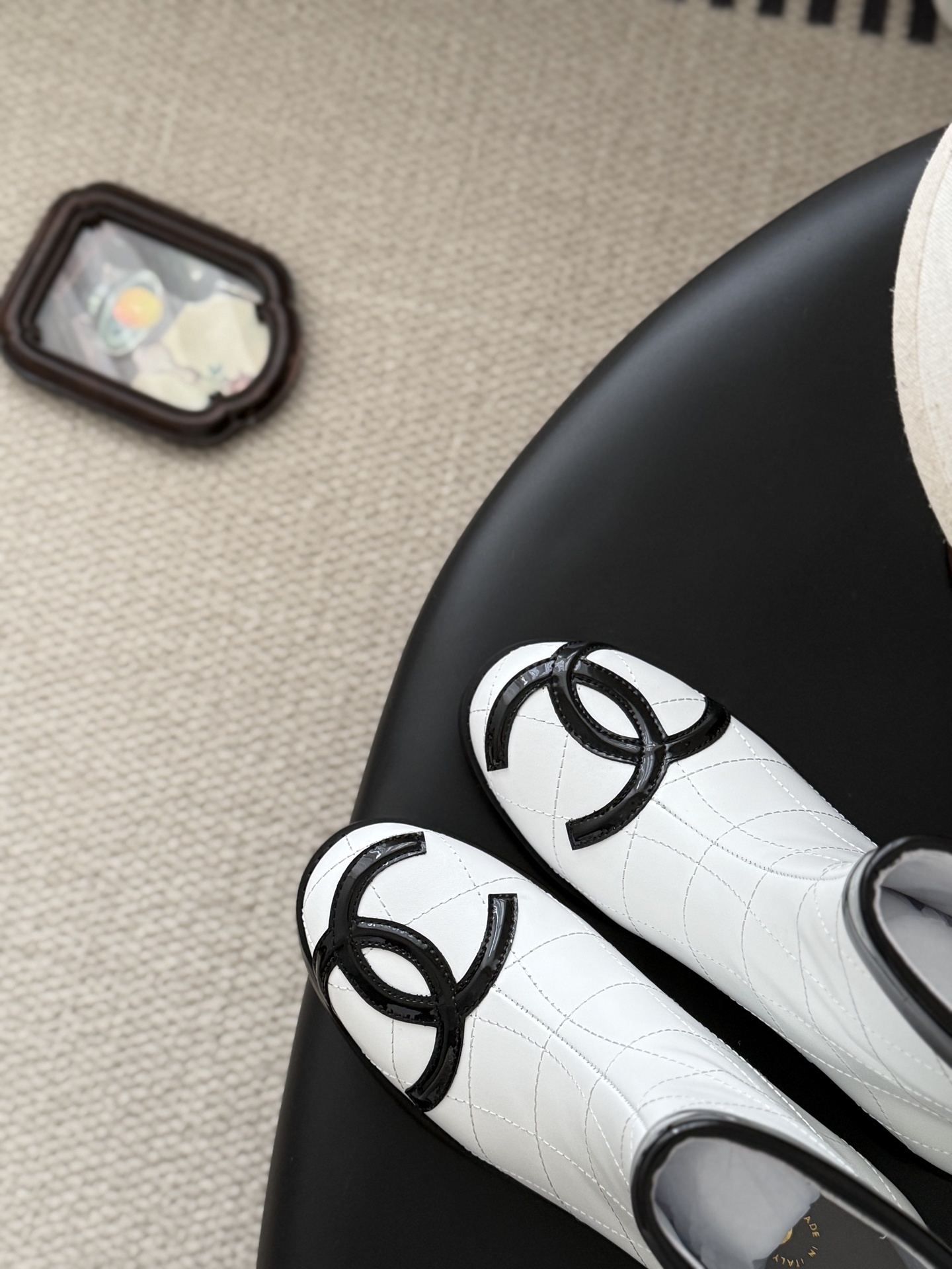 Pair of Chanel white quilted leather ankle boots with black patent leather toe caps and interlocking CC logos on a black surface. - Hình 7