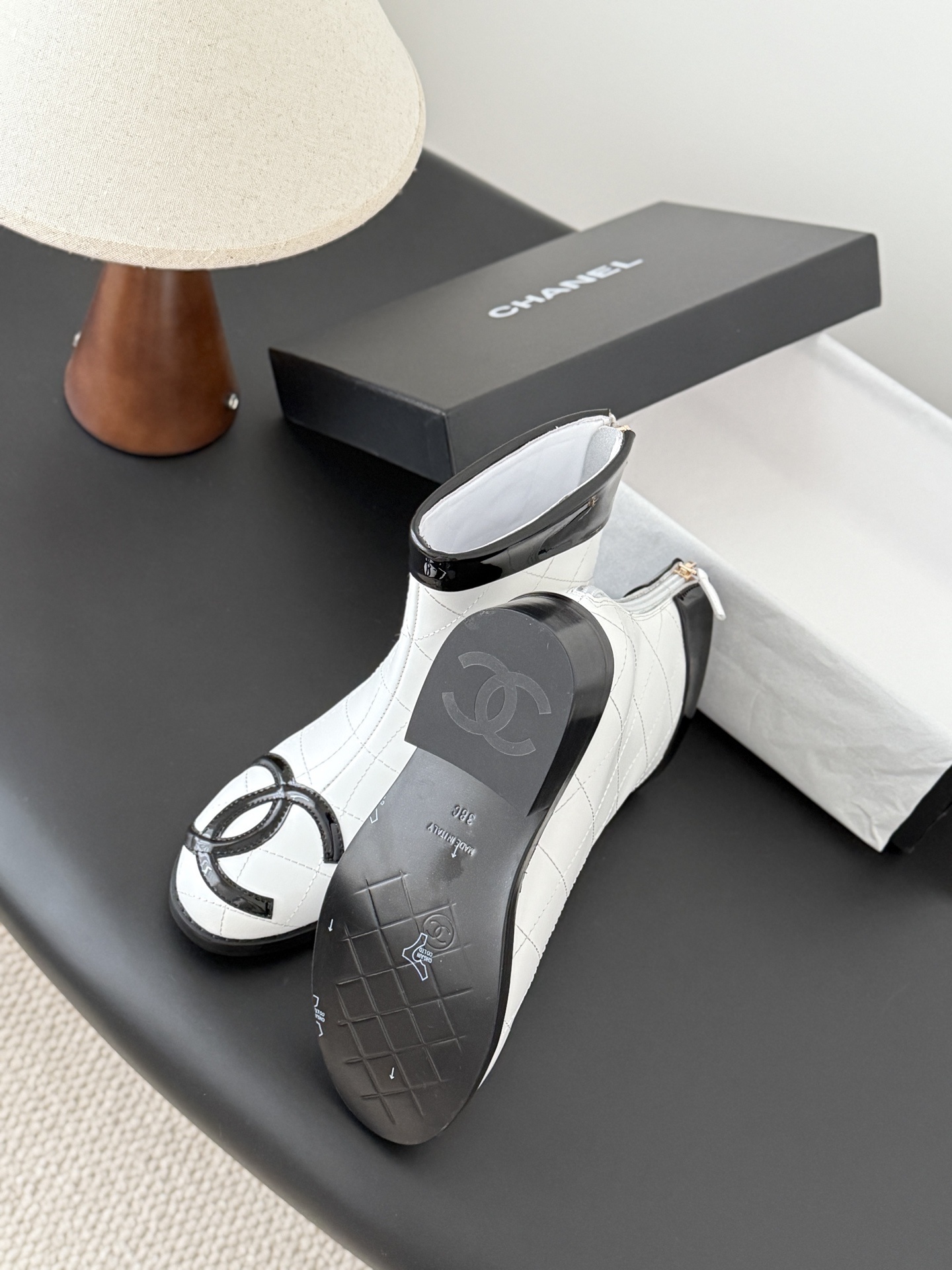 Pair of Chanel white quilted leather ankle boots with black patent leather toe caps and interlocking CC logos on a black surface. - Hình 5