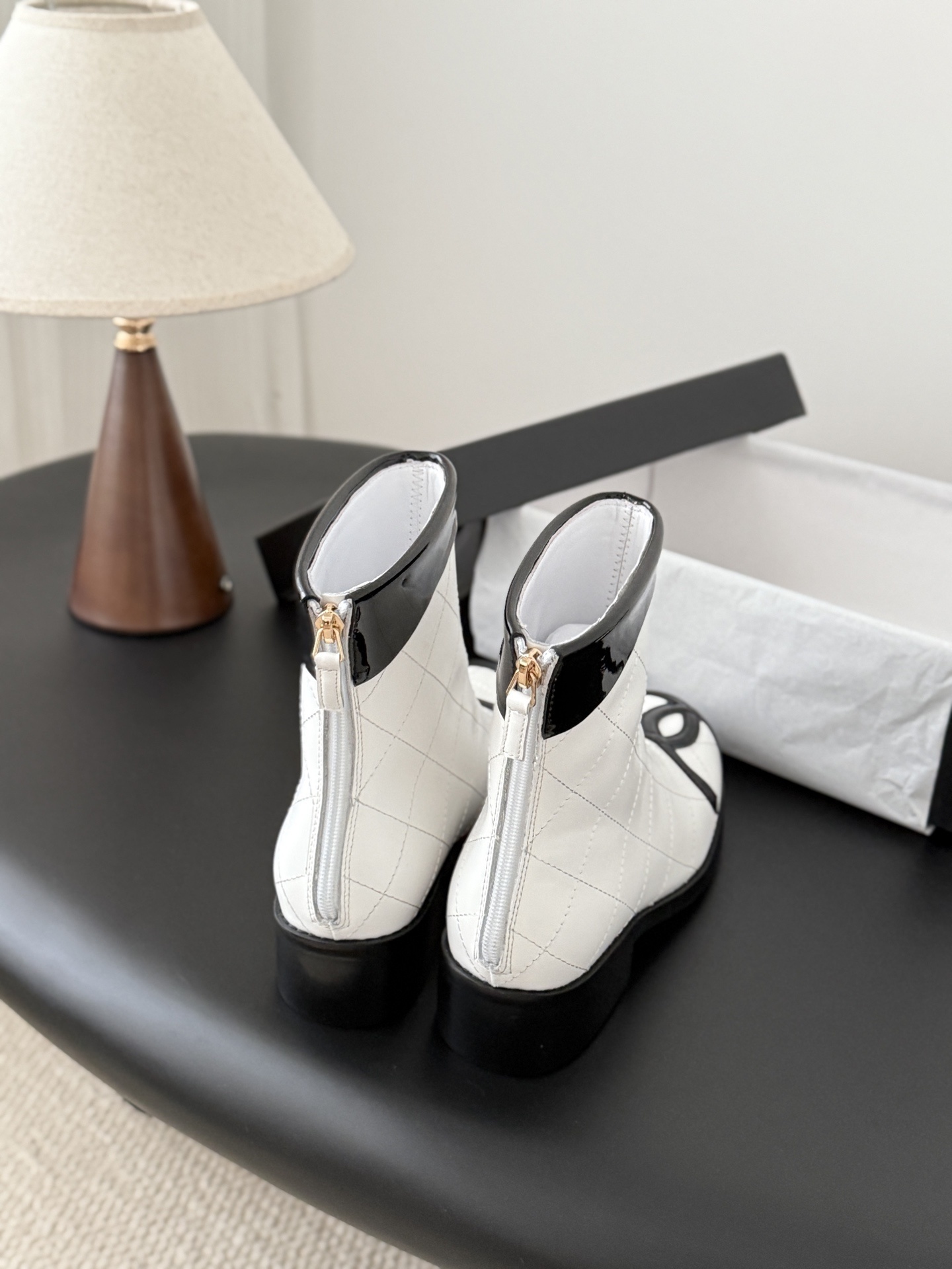 Pair of Chanel white quilted leather ankle boots with black patent leather toe caps and interlocking CC logos on a black surface. - Hình 3