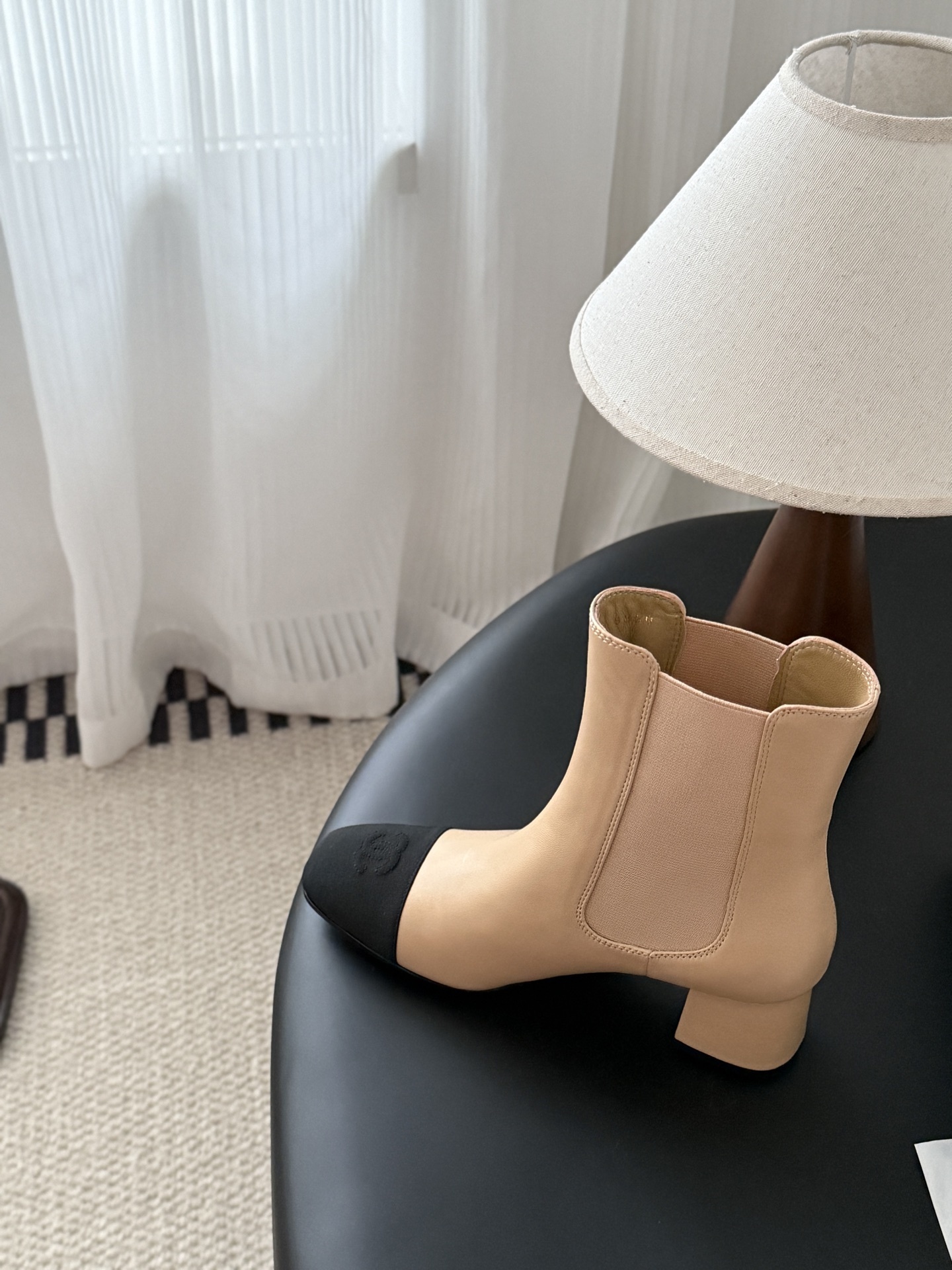 Chanel beige leather ankle boots with black toe caps and block heels displayed next to a black Chanel shoe box. - Hình 8