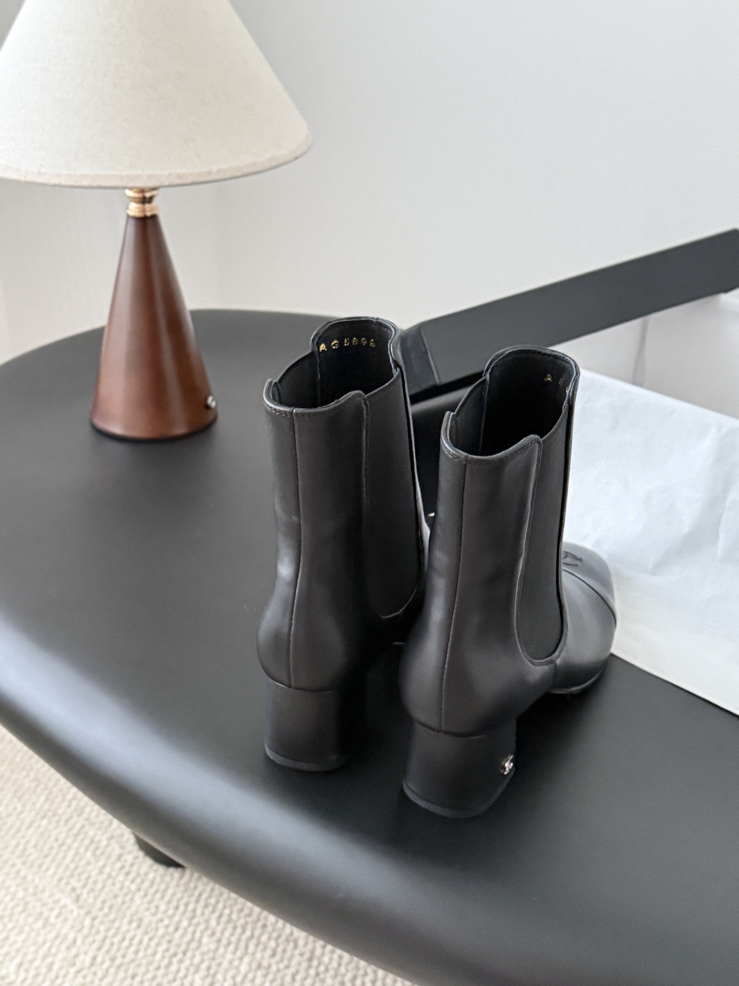 Pair of black Chanel leather ankle boots with patent leather cap toes and block heels displayed next to a Chanel shoe box. - Hình 3