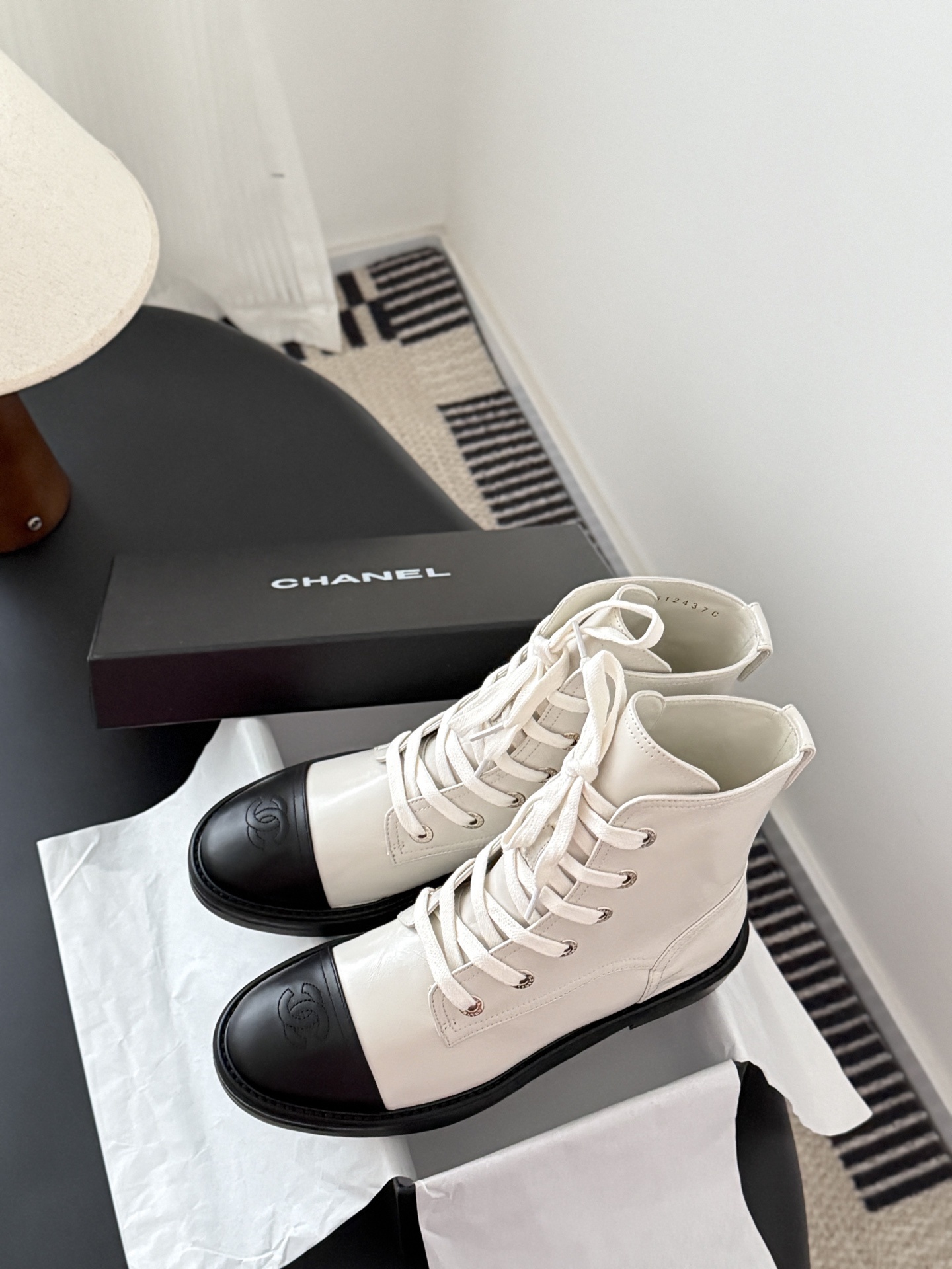 Chanel beige leather combat boots with black toe caps and gold CC logo on the heel next to a Chanel box. - Hình 9