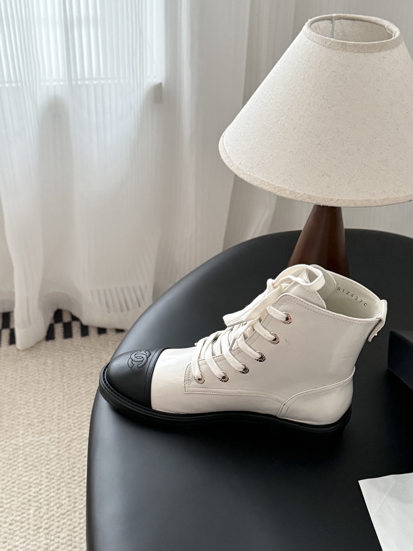 Chanel beige leather combat boots with black toe caps and gold CC logo on the heel next to a Chanel box. - Hình 8