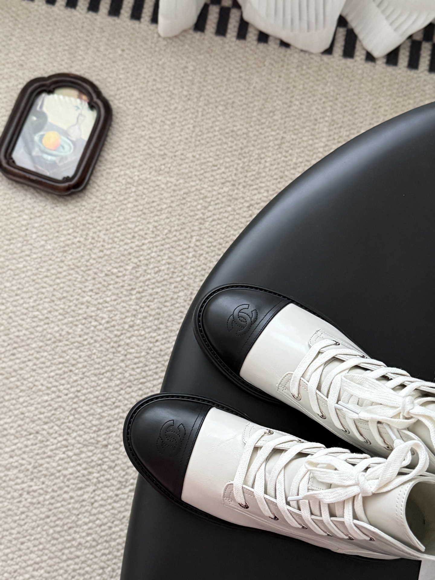 Chanel beige leather combat boots with black toe caps and gold CC logo on the heel next to a Chanel box. - Hình 7