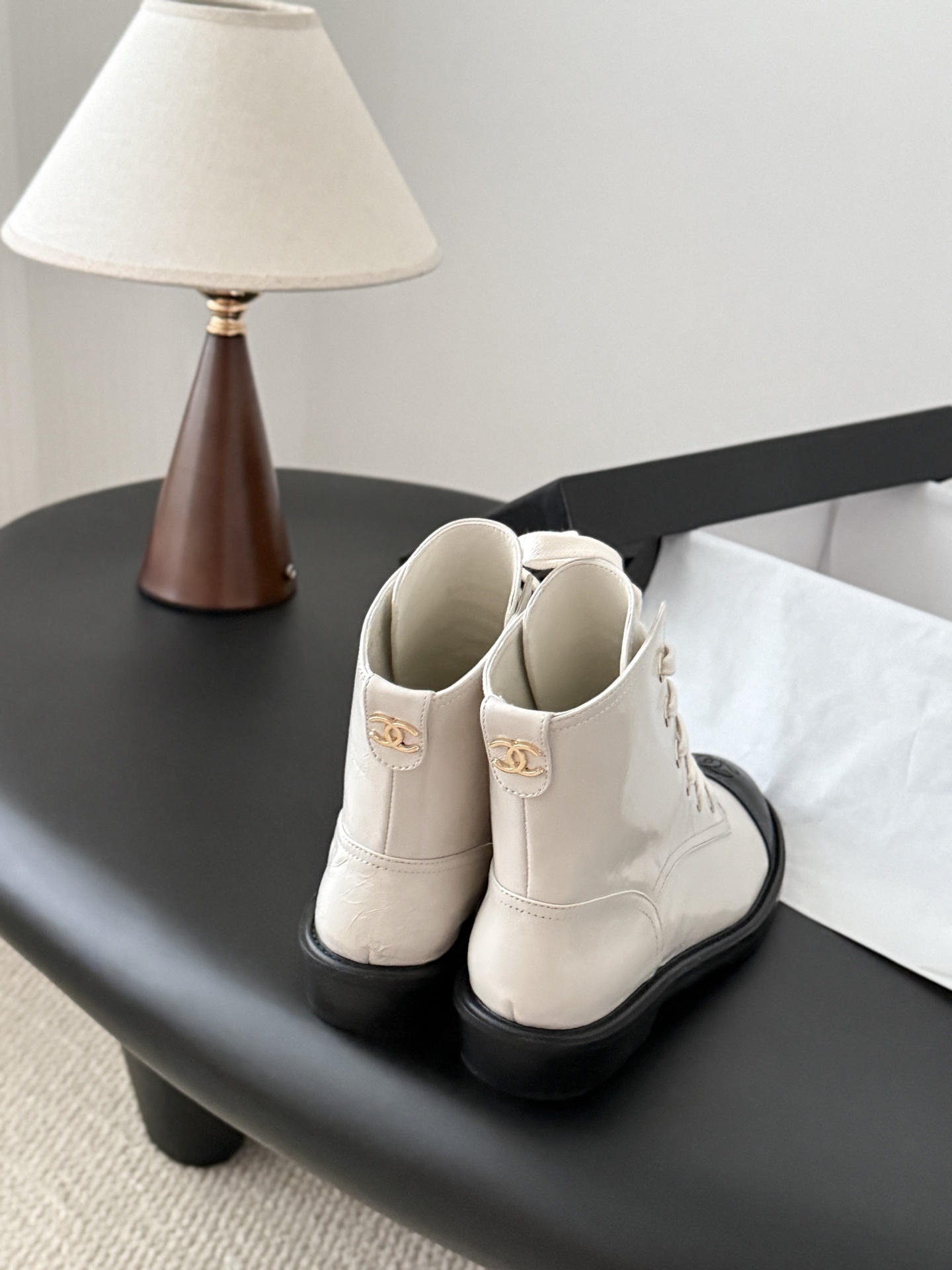Chanel beige leather combat boots with black toe caps and gold CC logo on the heel next to a Chanel box. - Hình 3
