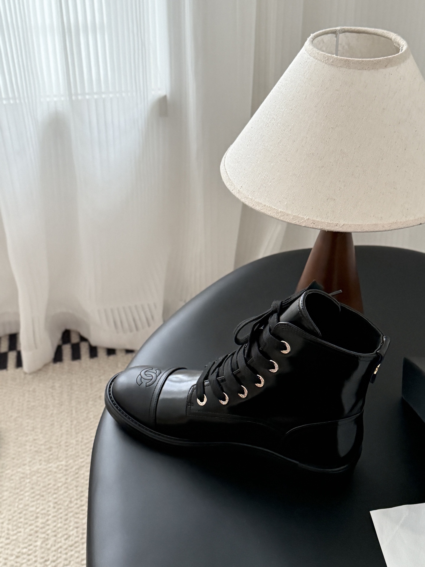 Pair of black Chanel patent leather lace-up combat boots with CC logo on toe and heel, displayed next to a Chanel shoebox on a black table. - Hình 8