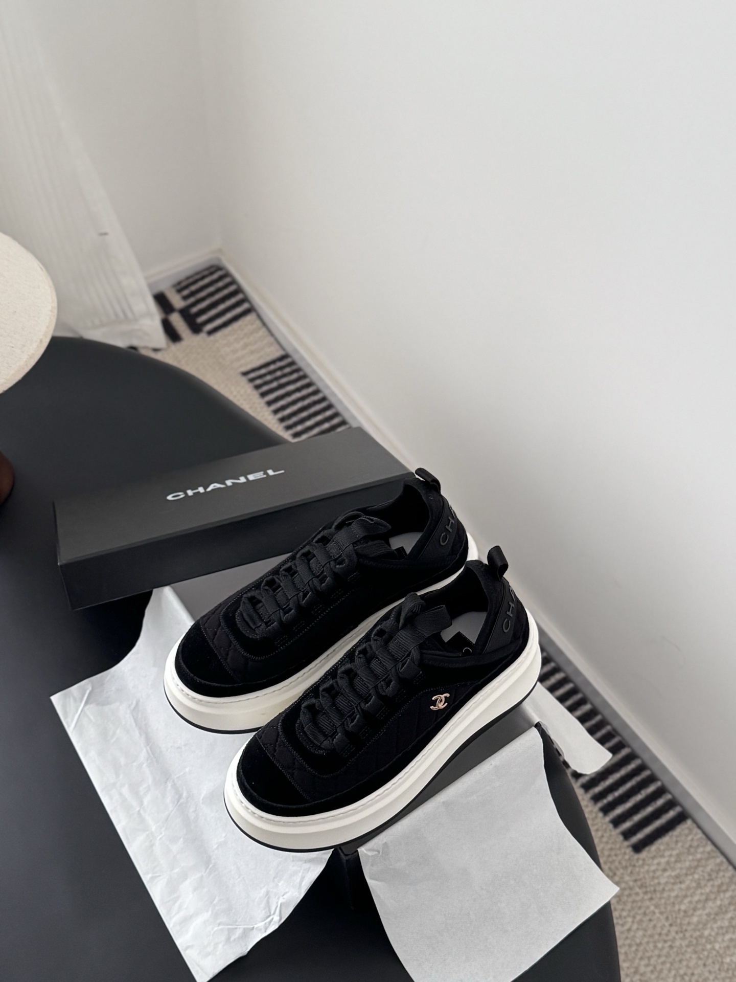 A pair of black Chanel quilted platform sneakers with white soles and gold CC logo next to a black Chanel shoe box. - Hình 6