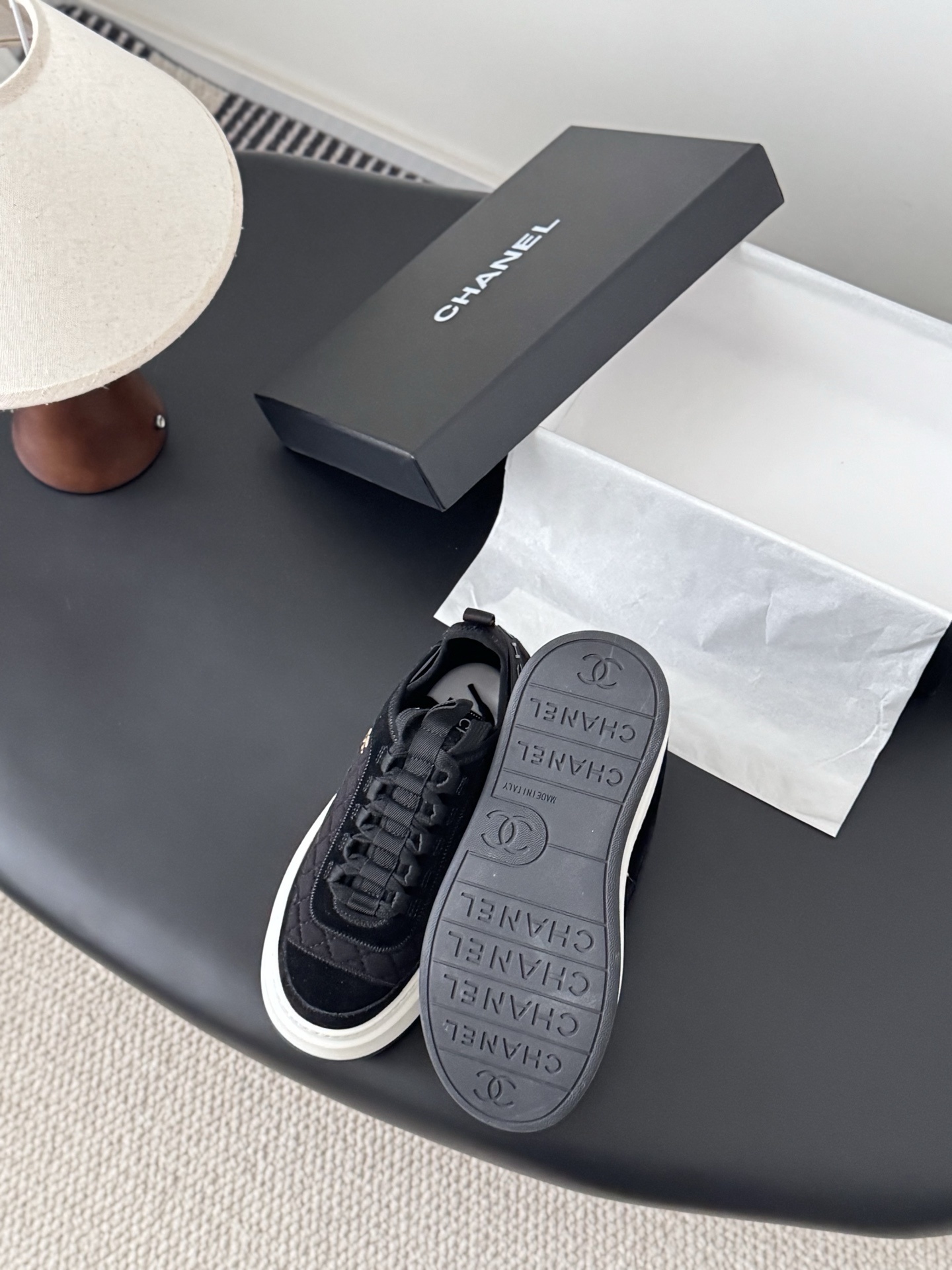 A pair of black Chanel quilted platform sneakers with white soles and gold CC logo next to a black Chanel shoe box. - Hình 4
