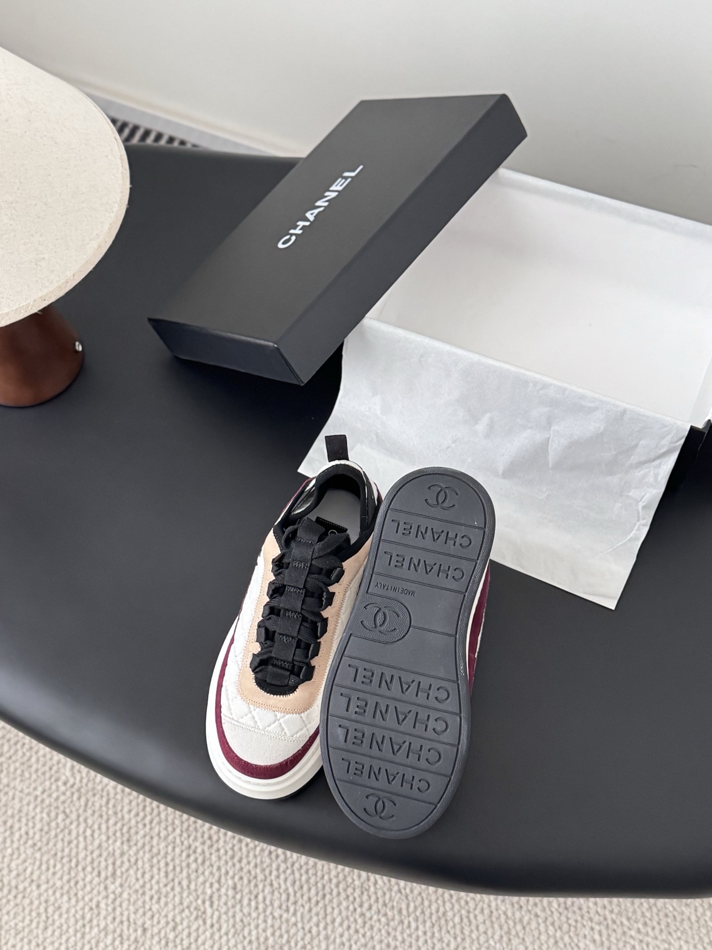 A pair of Chanel white quilted leather platform sneakers with burgundy and beige suede accents sitting next to a black Chanel shoe box. - Hình 4