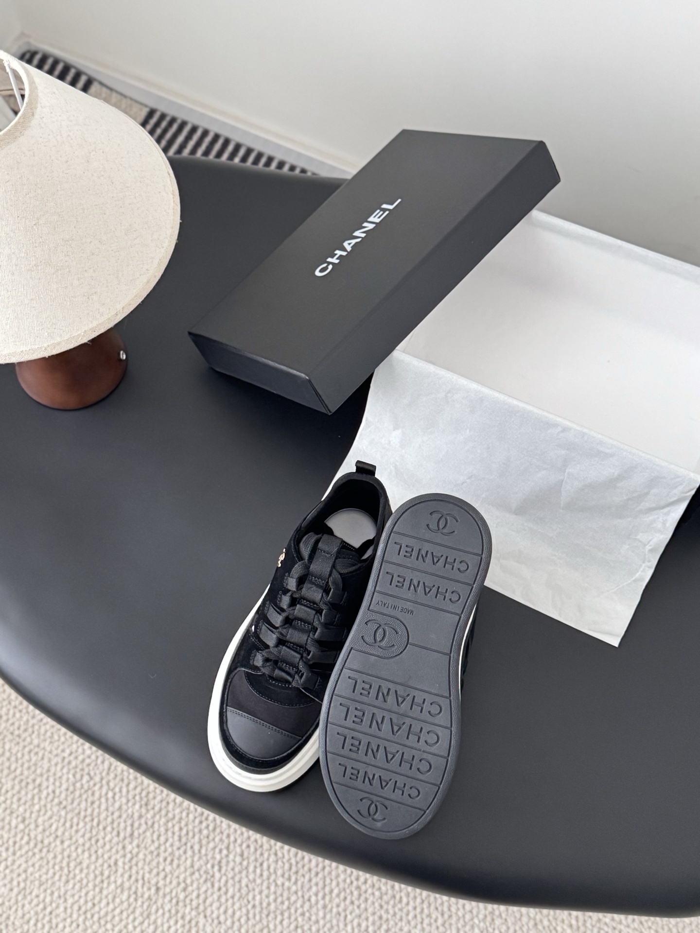 A pair of Chanel black suede and fabric sneakers with chunky white platform soles and gold CC logo next to a branded Chanel box. - Hình 4