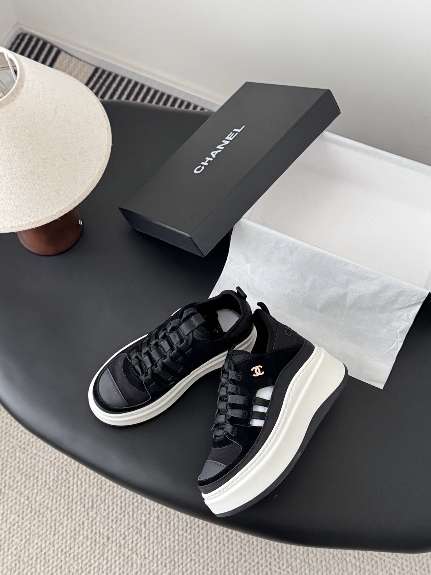 A pair of Chanel black suede and fabric sneakers with chunky white platform soles and gold CC logo next to a branded Chanel box. - Hình 3