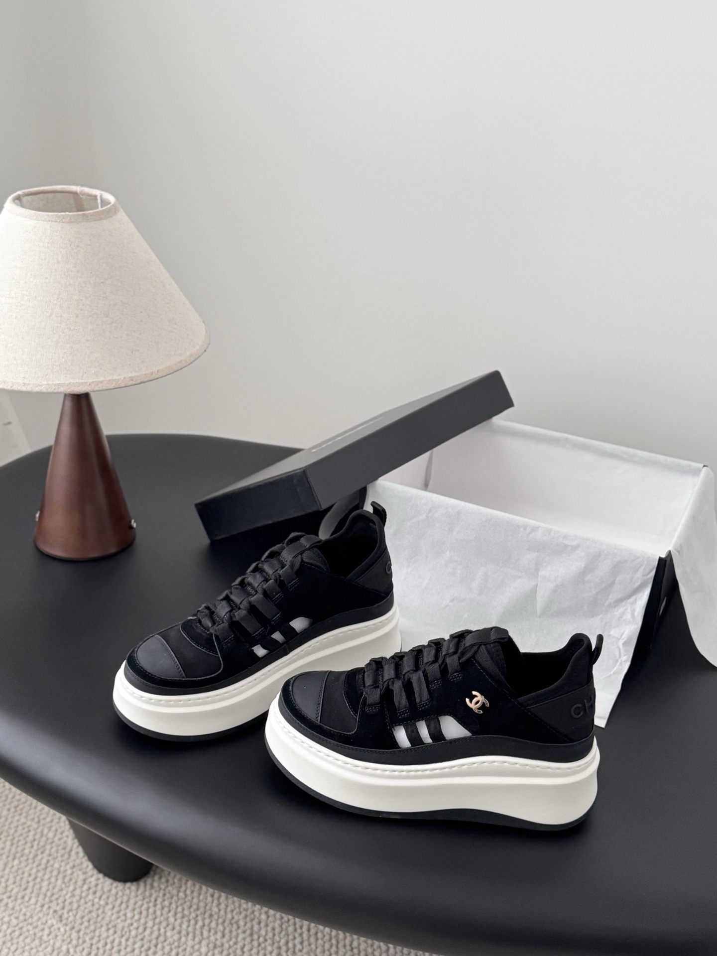 A pair of Chanel black suede and fabric sneakers with chunky white platform soles and gold CC logo next to a branded Chanel box. - Hình 2