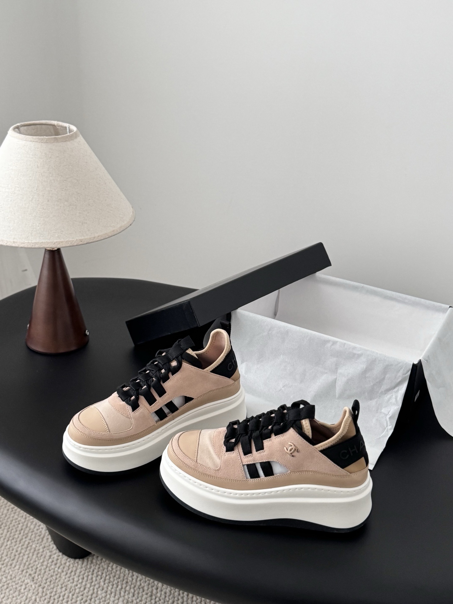 Chanel beige and black leather platform sneakers with chunky white soles displayed next to a black Chanel shoe box. - Hình 2
