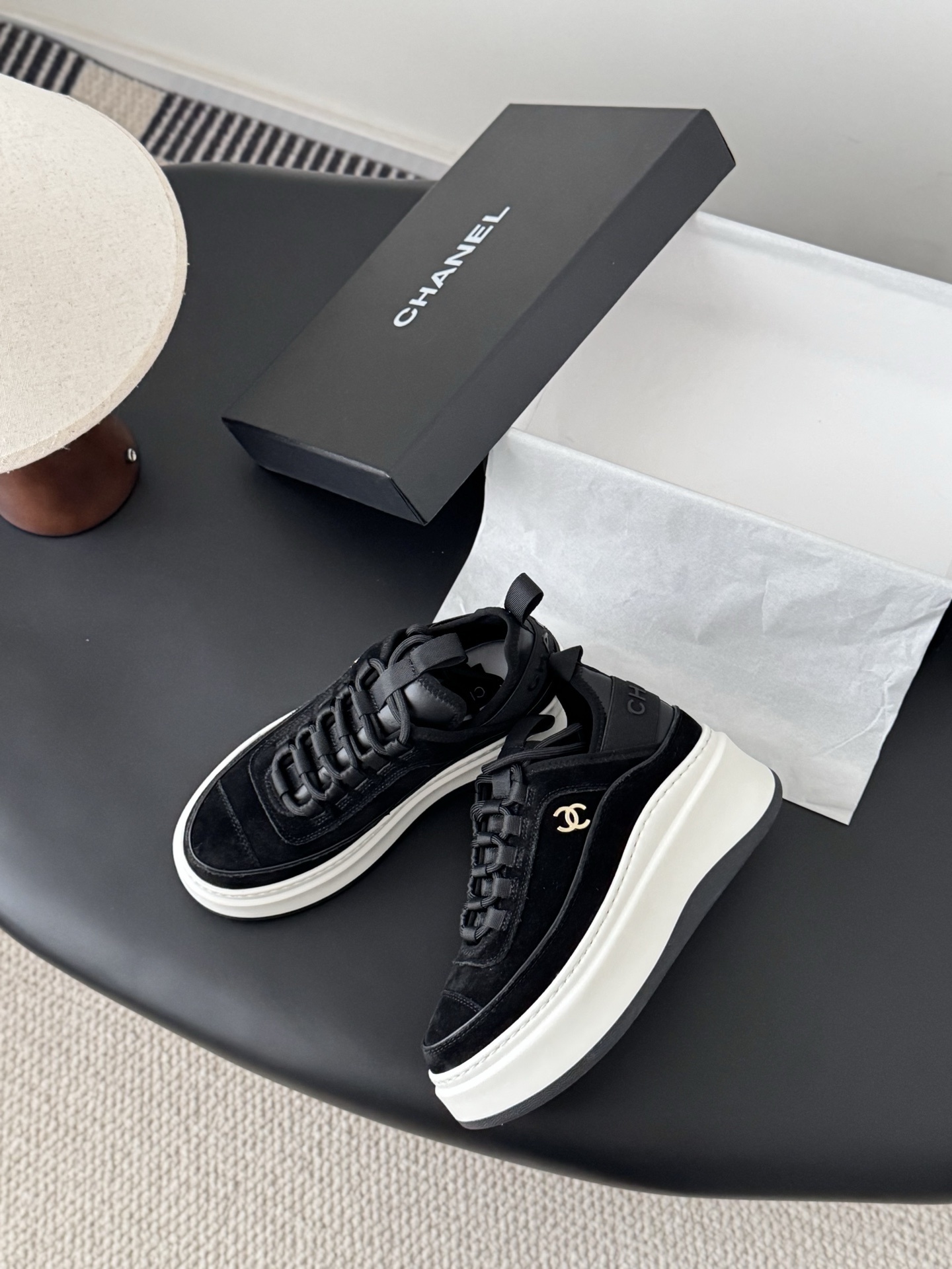 Pair of black Chanel suede platform sneakers with chunky white soles and gold CC logo next to a Chanel shoe box - Hình 3