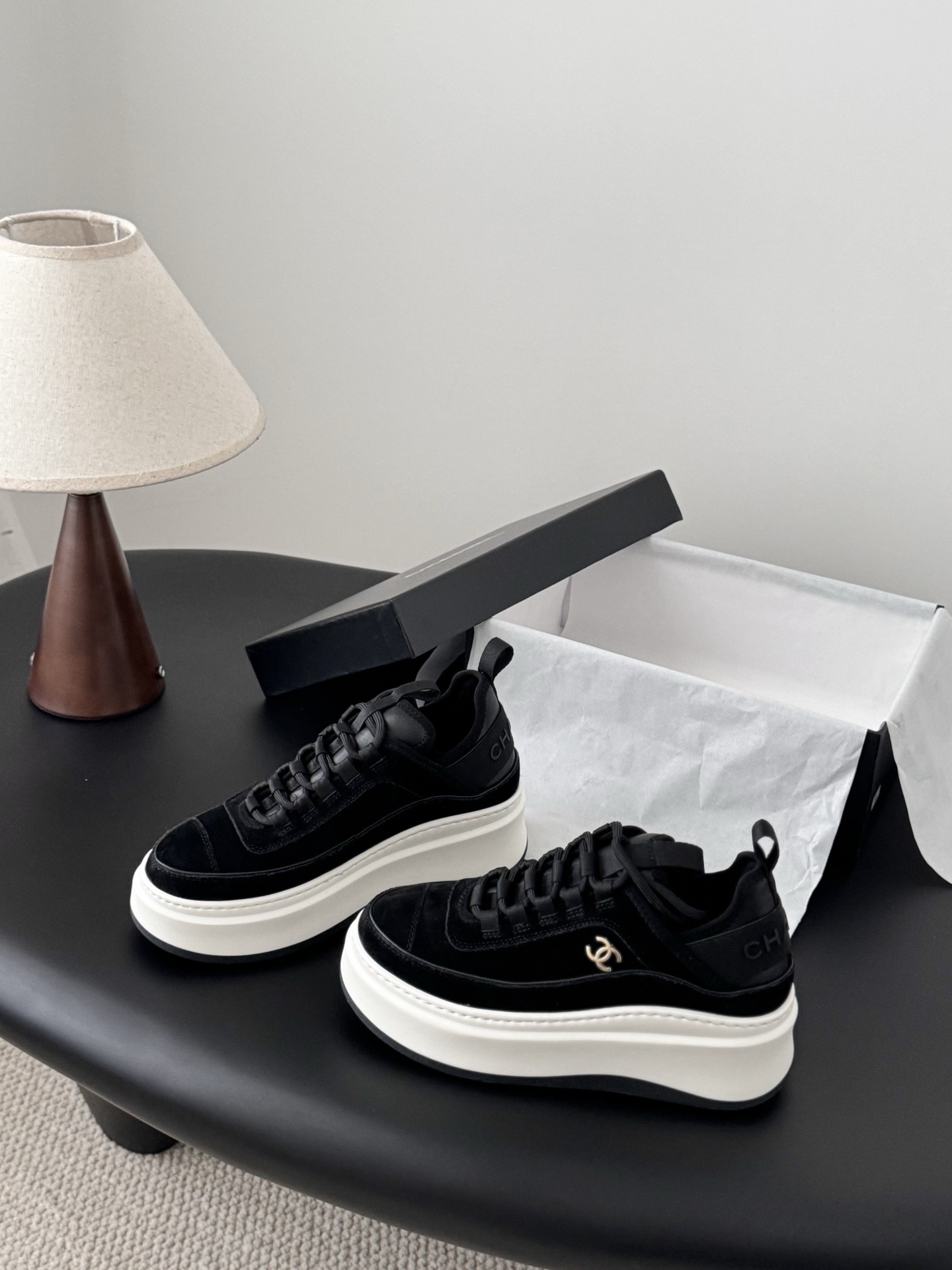 Pair of black Chanel suede platform sneakers with chunky white soles and gold CC logo next to a Chanel shoe box - Hình 2