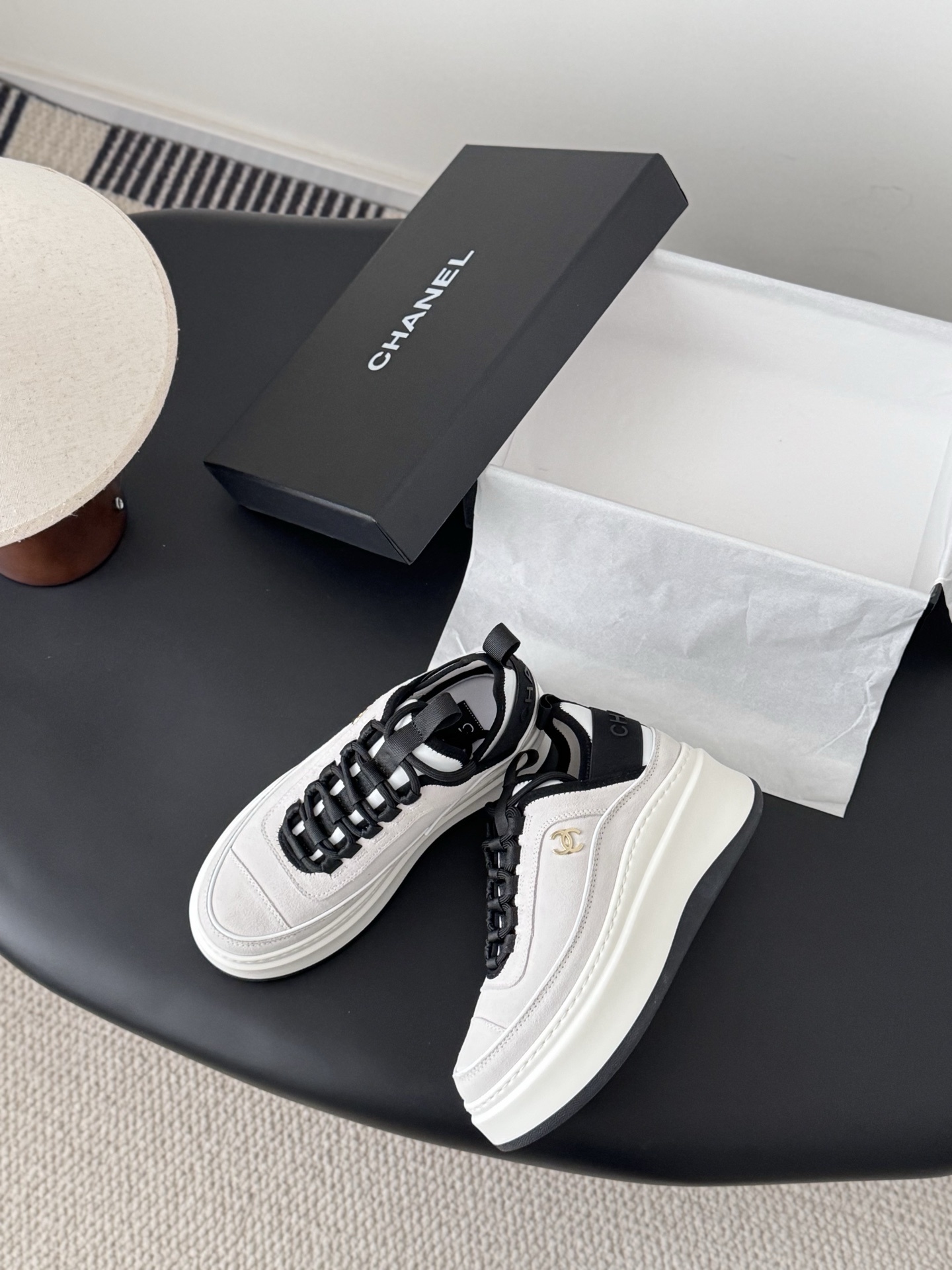 Luxury Chanel platform sneakers in off-white and black with gold CC logo detail on a black table with box. - Hình 3