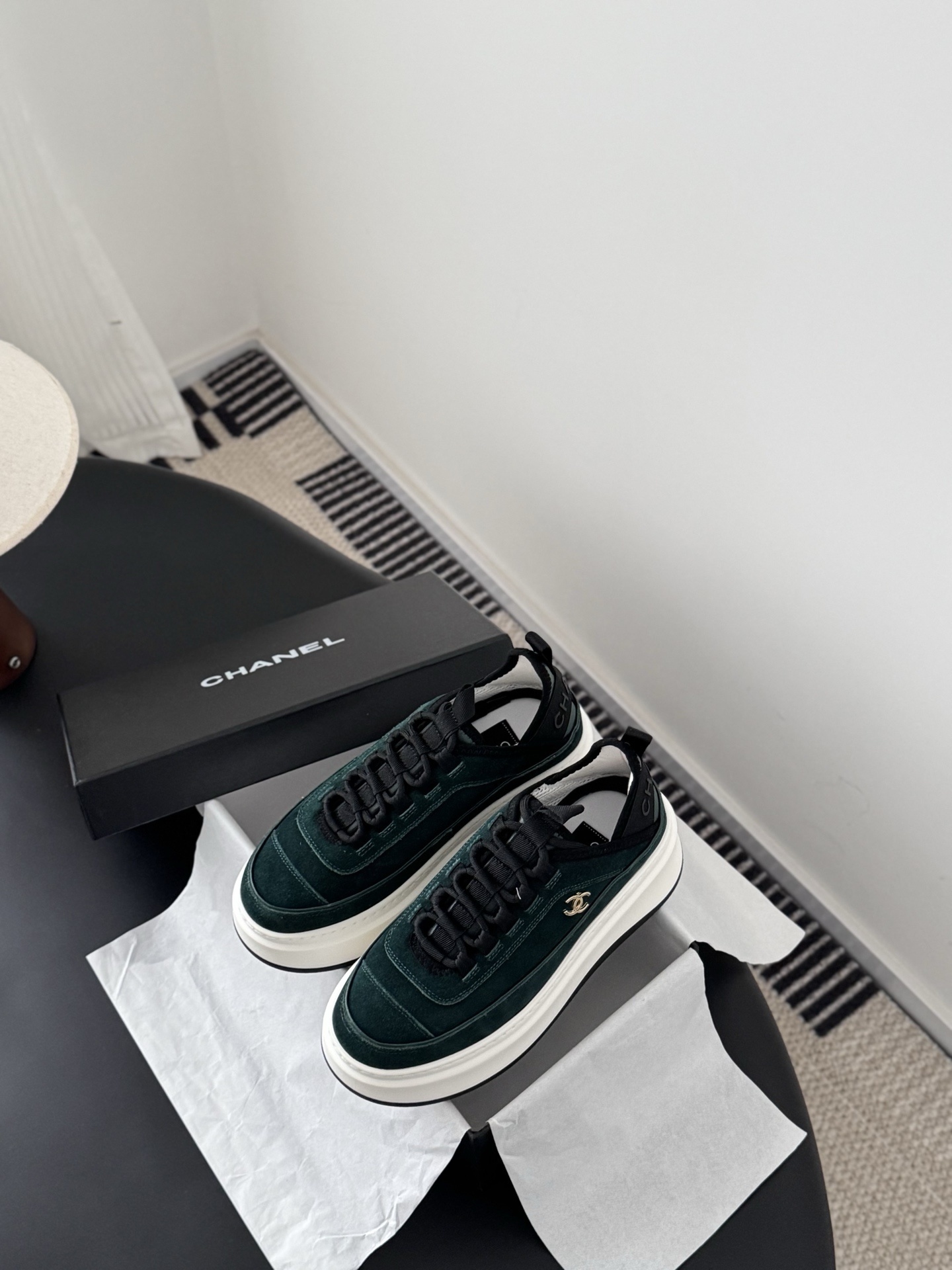 A pair of Chanel dark green suede sneakers with white platform soles and gold CC logos placed next to a black Chanel shoebox on a table. - Hình 6