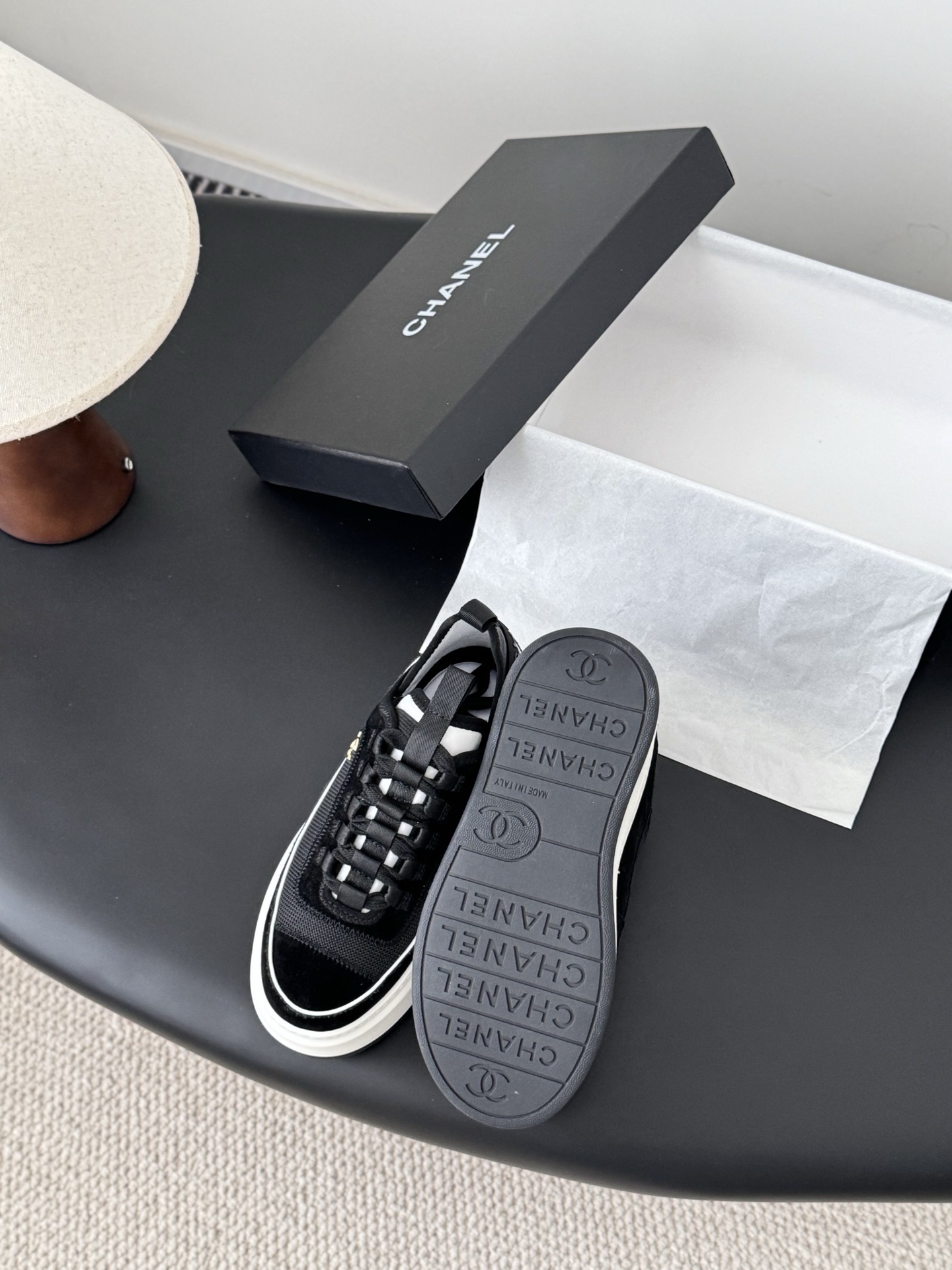Pair of Chanel black mesh and suede platform sneakers with white soles and gold CC logo on a black table next to a Chanel box - Hình 4