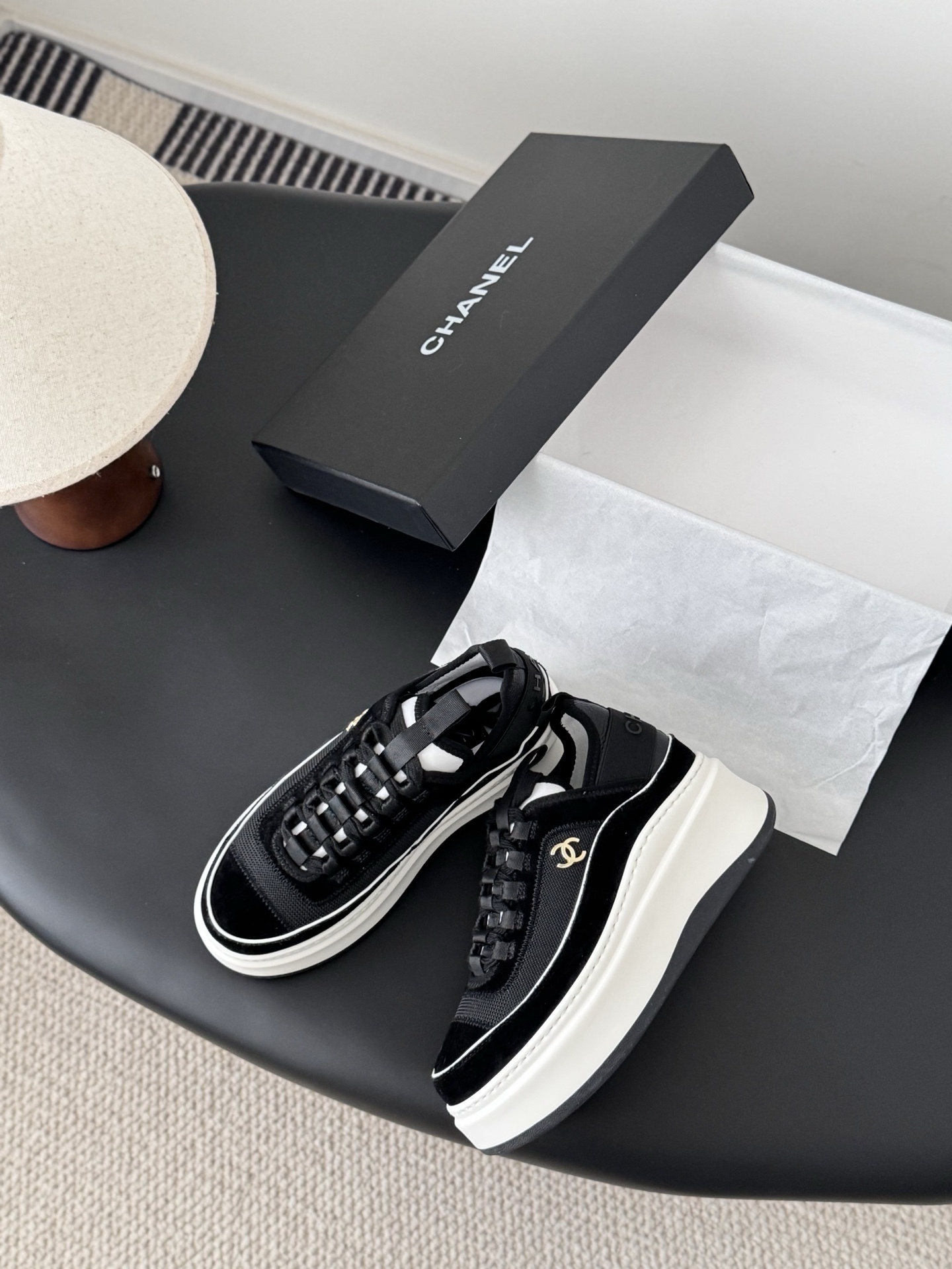 Pair of Chanel black mesh and suede platform sneakers with white soles and gold CC logo on a black table next to a Chanel box - Hình 3