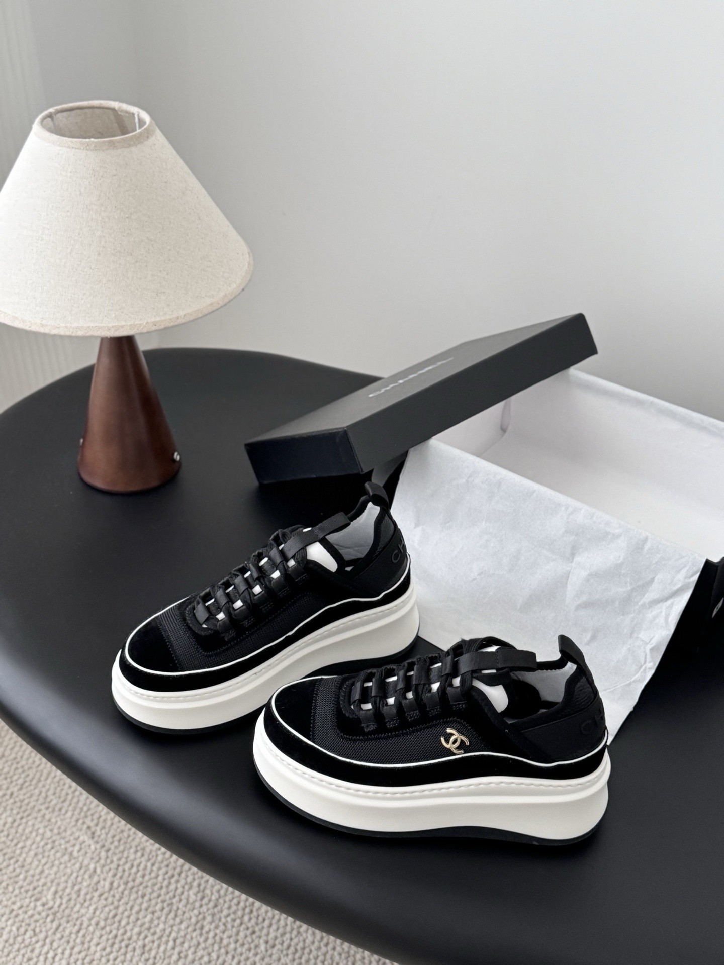 Pair of Chanel black mesh and suede platform sneakers with white soles and gold CC logo on a black table next to a Chanel box - Hình 2