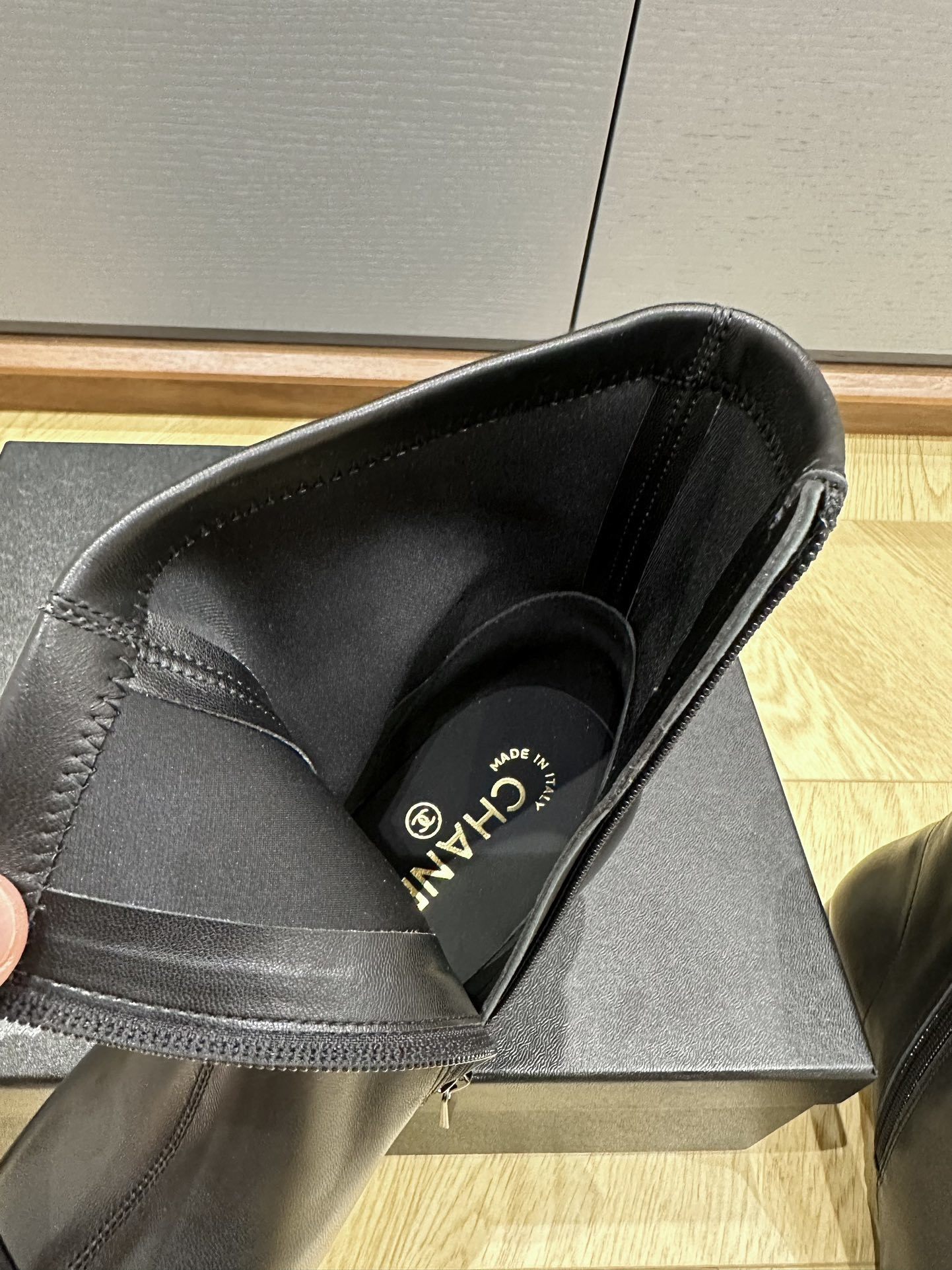 A pair of Chanel black leather ankle boots with grosgrain cap toes and silver CC logo on the block heel, displayed on a Chanel shoe box. - Hình 9