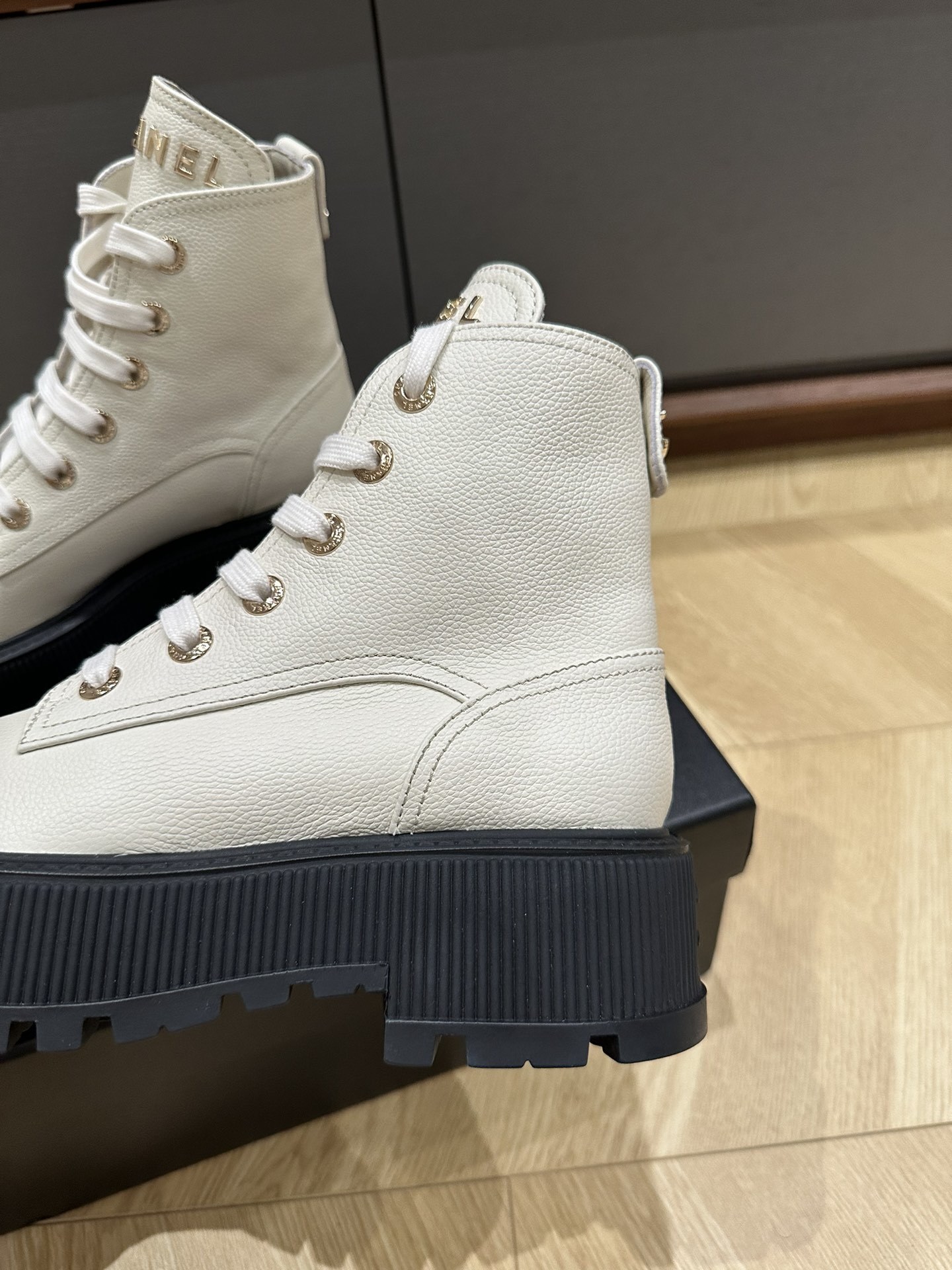 A pair of Chanel ivory grained leather combat boots with black patent toe caps and chunky platform soles on a black designer box. - Hình 7