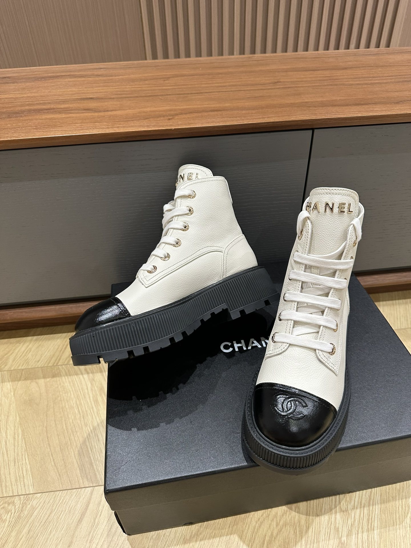 A pair of Chanel ivory grained leather combat boots with black patent toe caps and chunky platform soles on a black designer box. - Hình 6