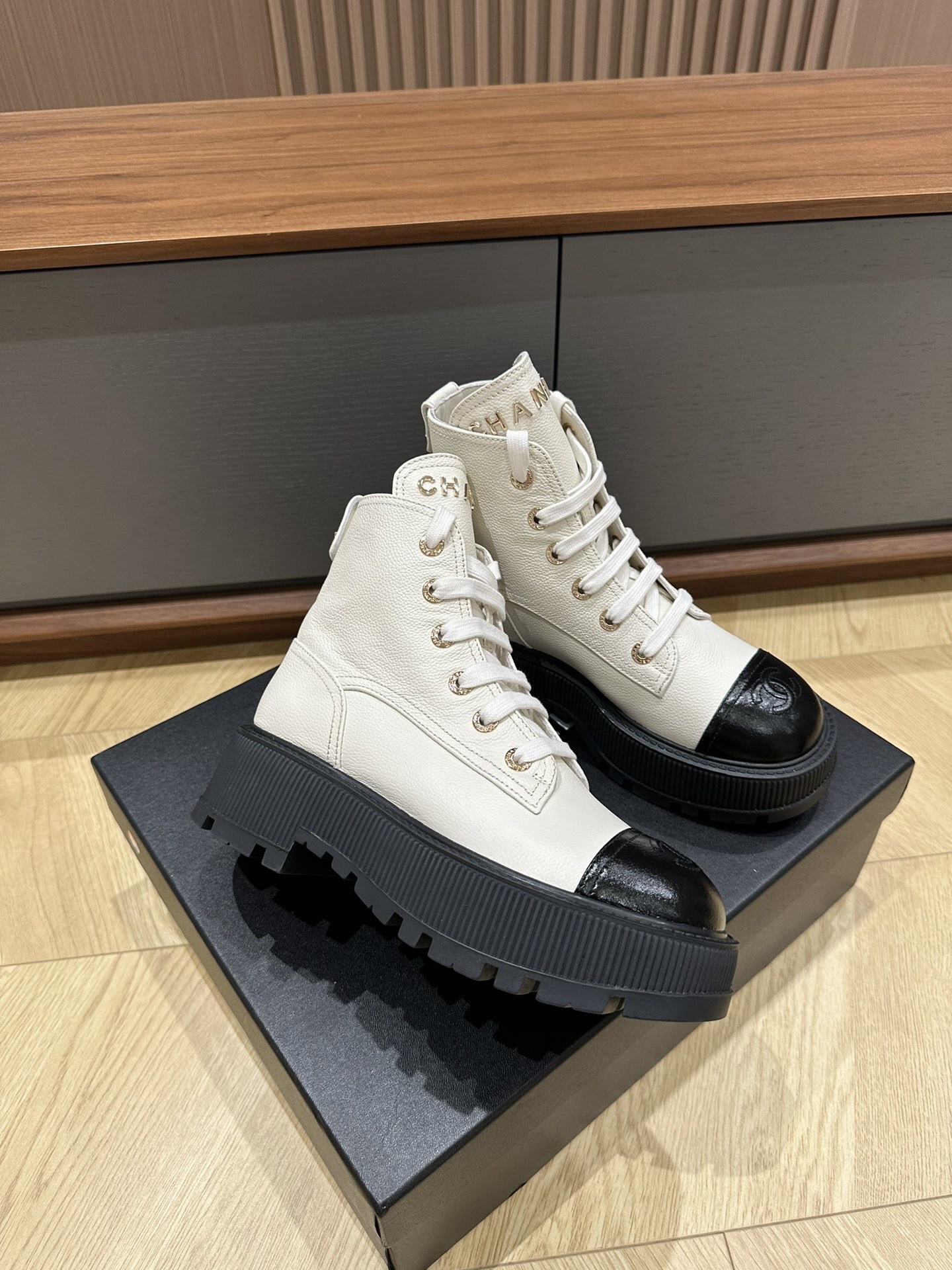 A pair of Chanel ivory grained leather combat boots with black patent toe caps and chunky platform soles on a black designer box. - Hình 4