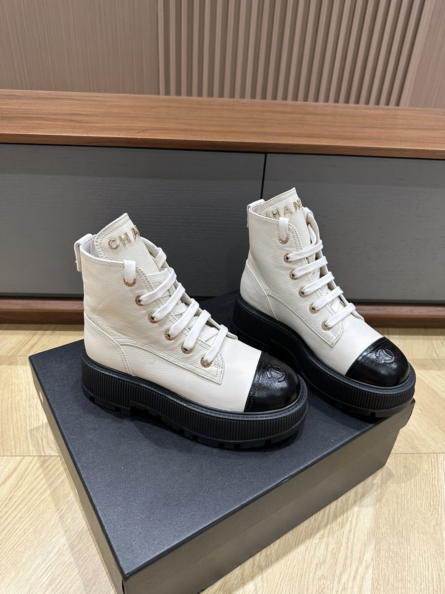 A pair of Chanel ivory grained leather combat boots with black patent toe caps and chunky platform soles on a black designer box. - Hình 3
