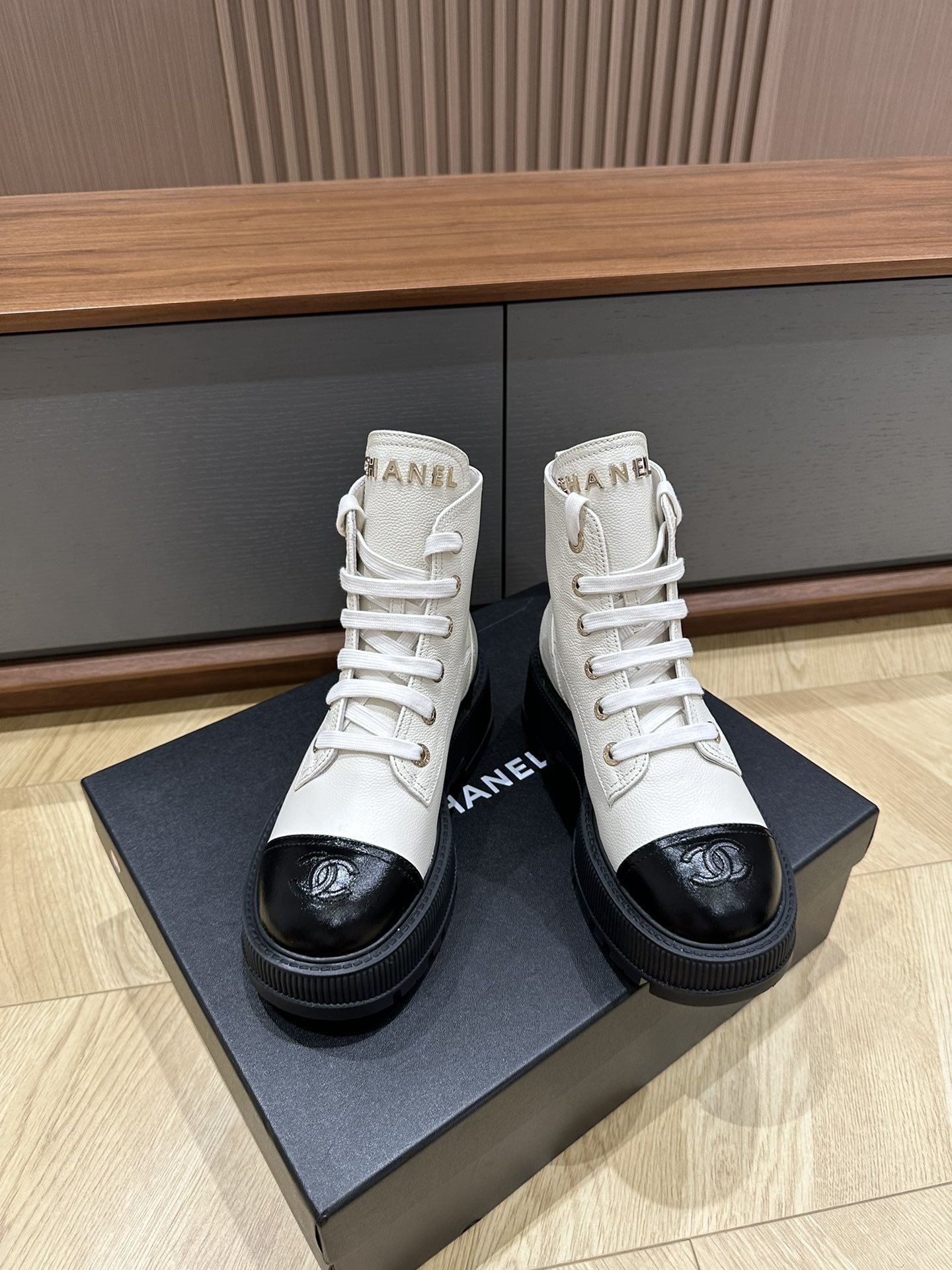 A pair of Chanel ivory grained leather combat boots with black patent toe caps and chunky platform soles on a black designer box. - Hình 2