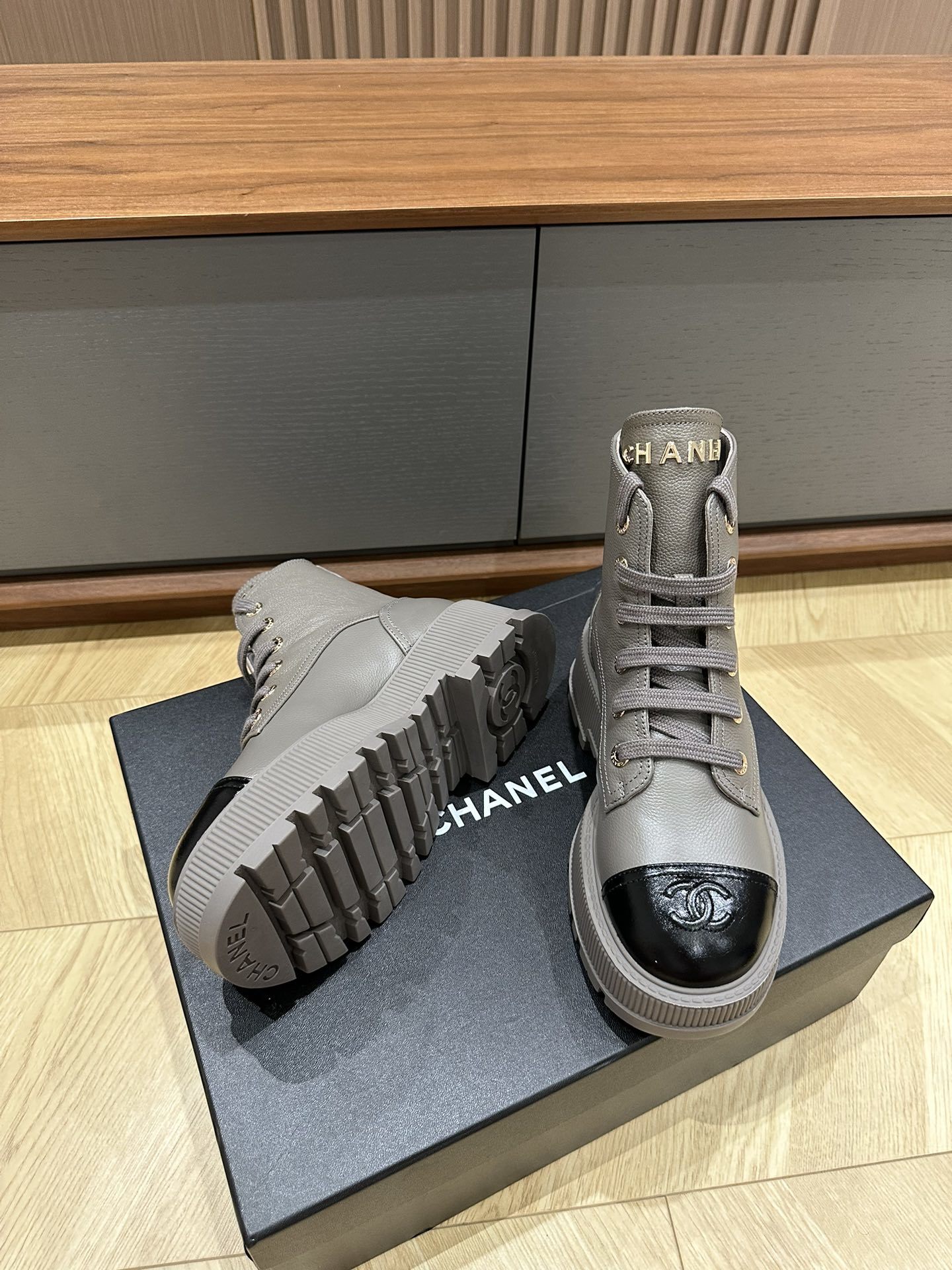Luxury Chanel grey leather ankle boots with black patent toe cap and gold brand lettering on a black box. - Hình 8
