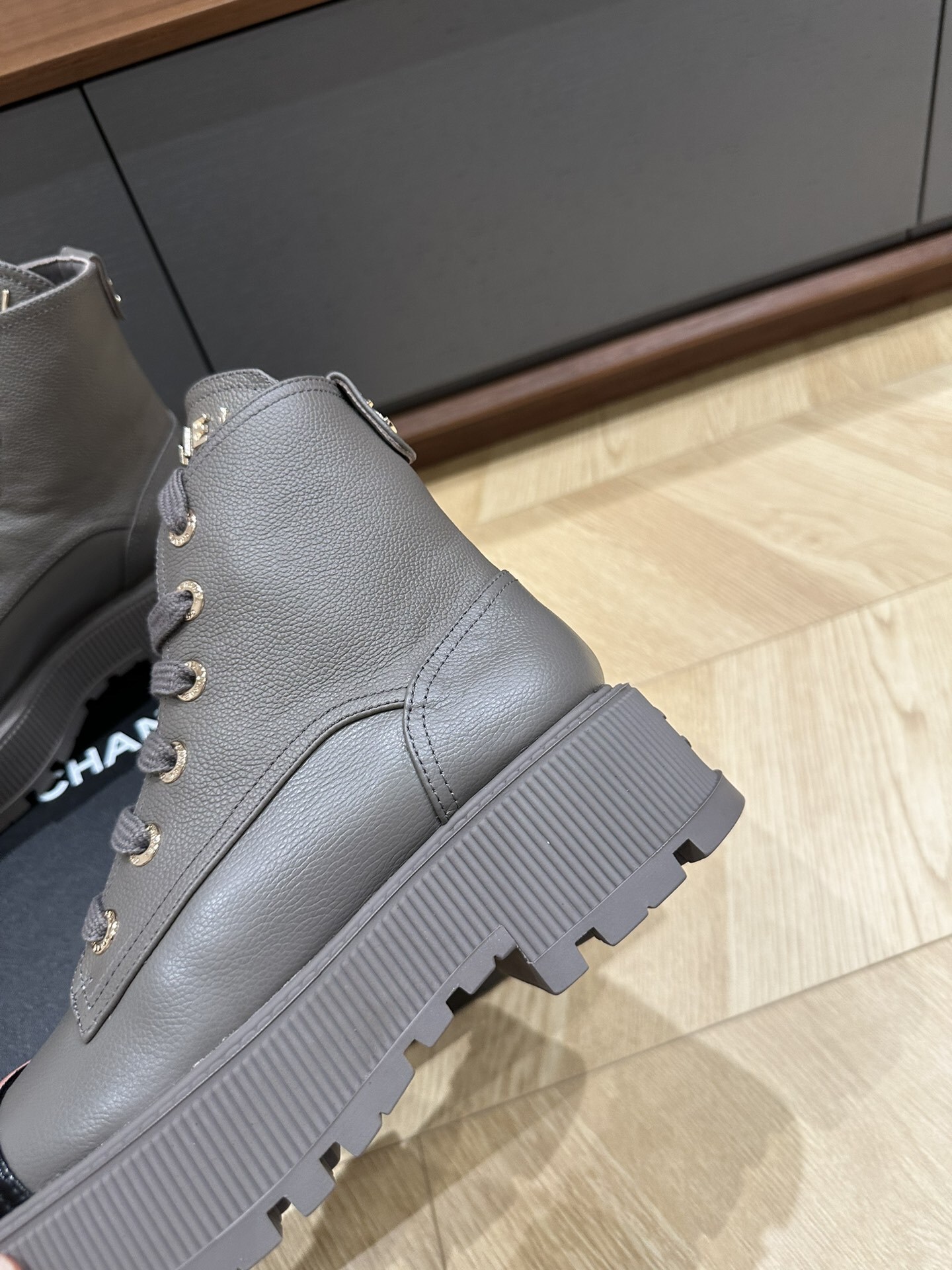 Luxury Chanel grey leather ankle boots with black patent toe cap and gold brand lettering on a black box. - Hình 6