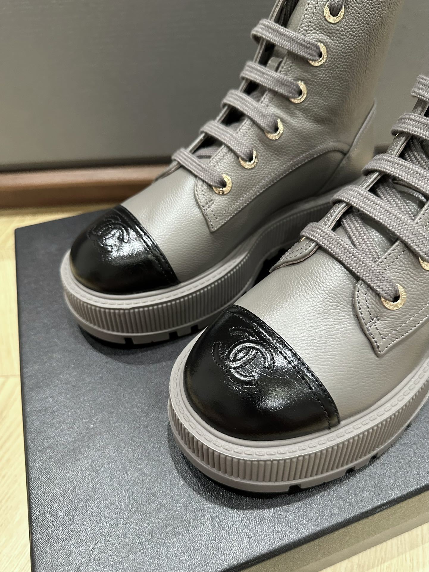 Luxury Chanel grey leather ankle boots with black patent toe cap and gold brand lettering on a black box. - Hình 5