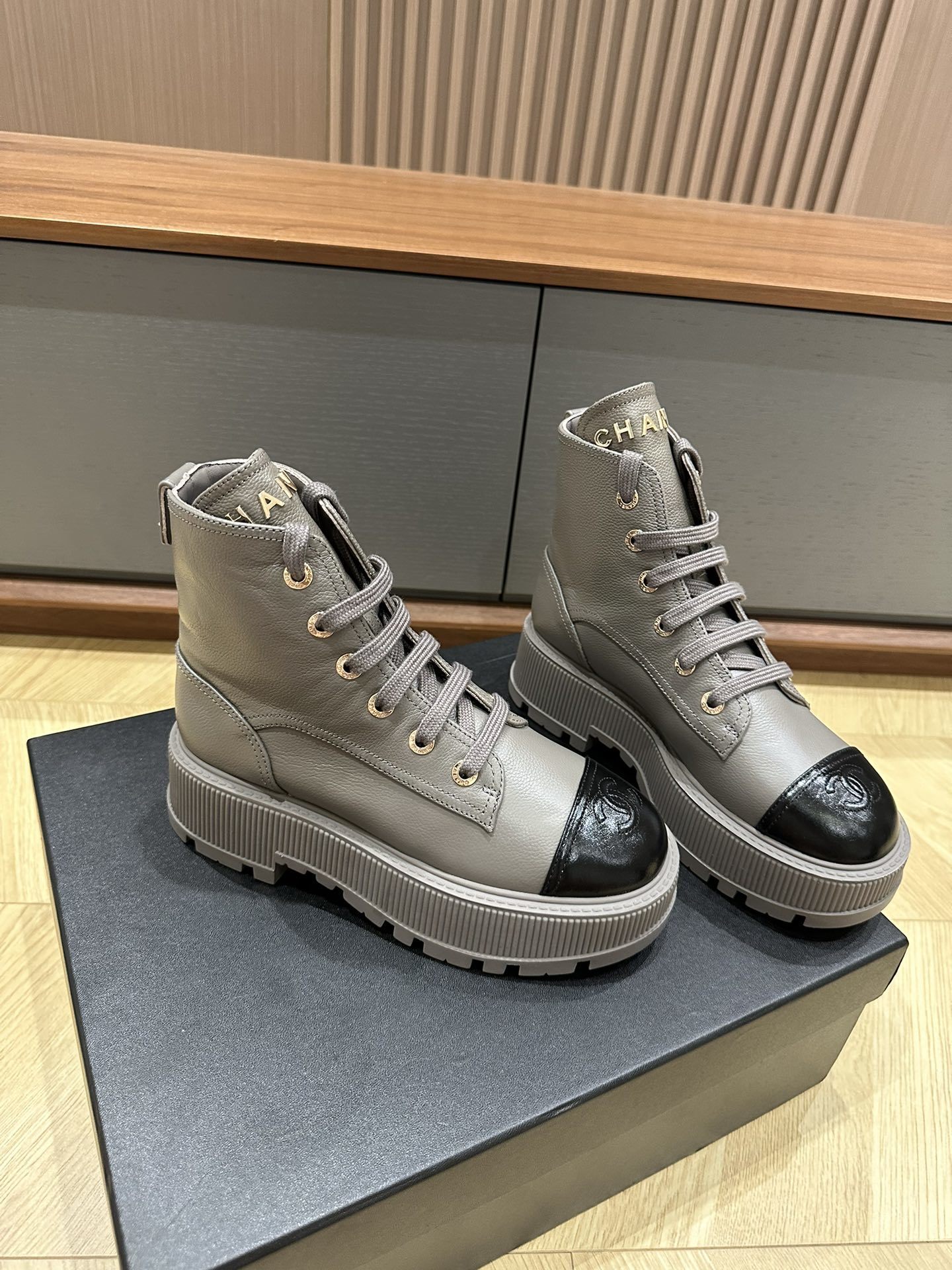 Luxury Chanel grey leather ankle boots with black patent toe cap and gold brand lettering on a black box. - Hình 3