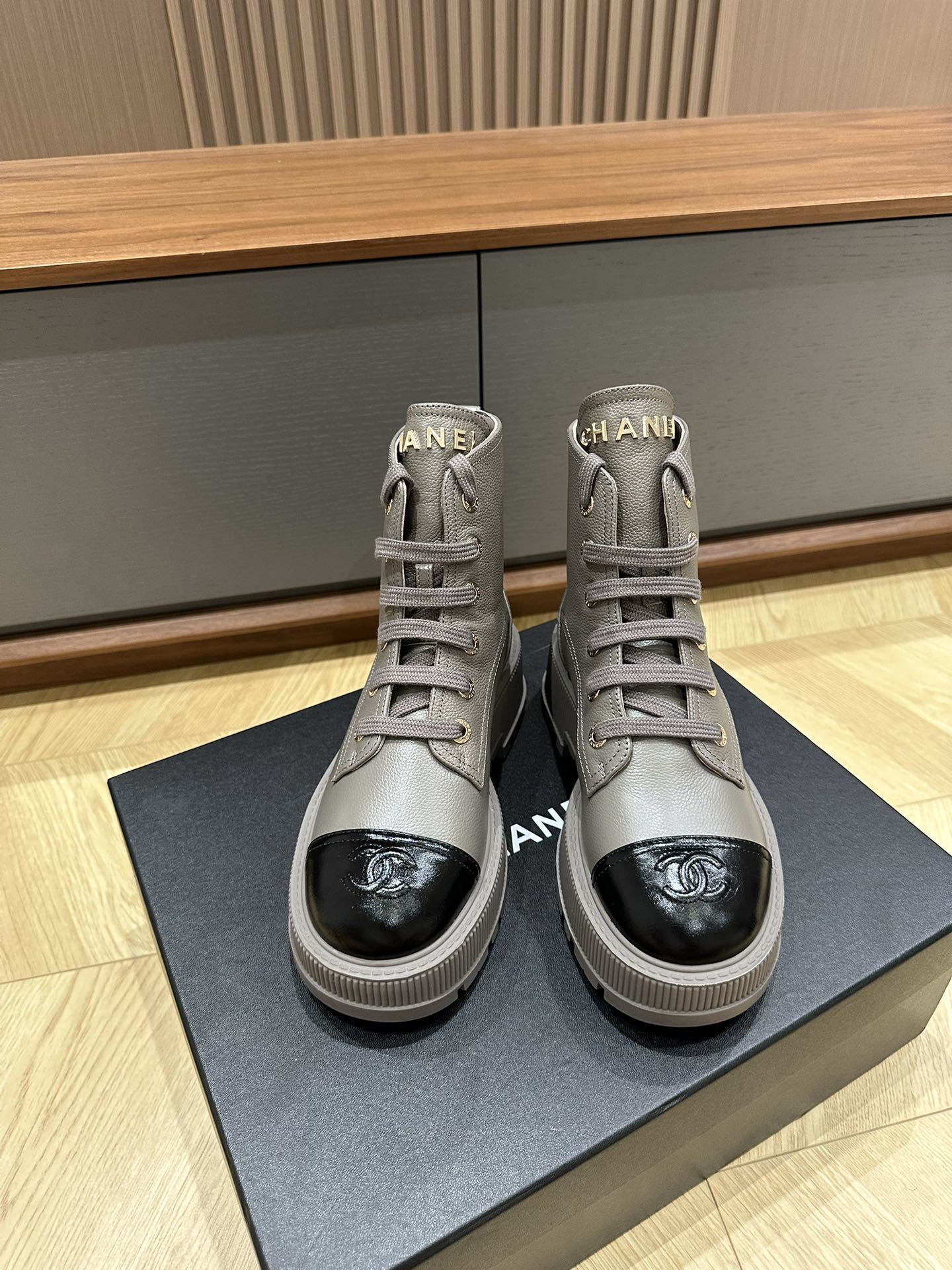 Luxury Chanel grey leather ankle boots with black patent toe cap and gold brand lettering on a black box. - Hình 2