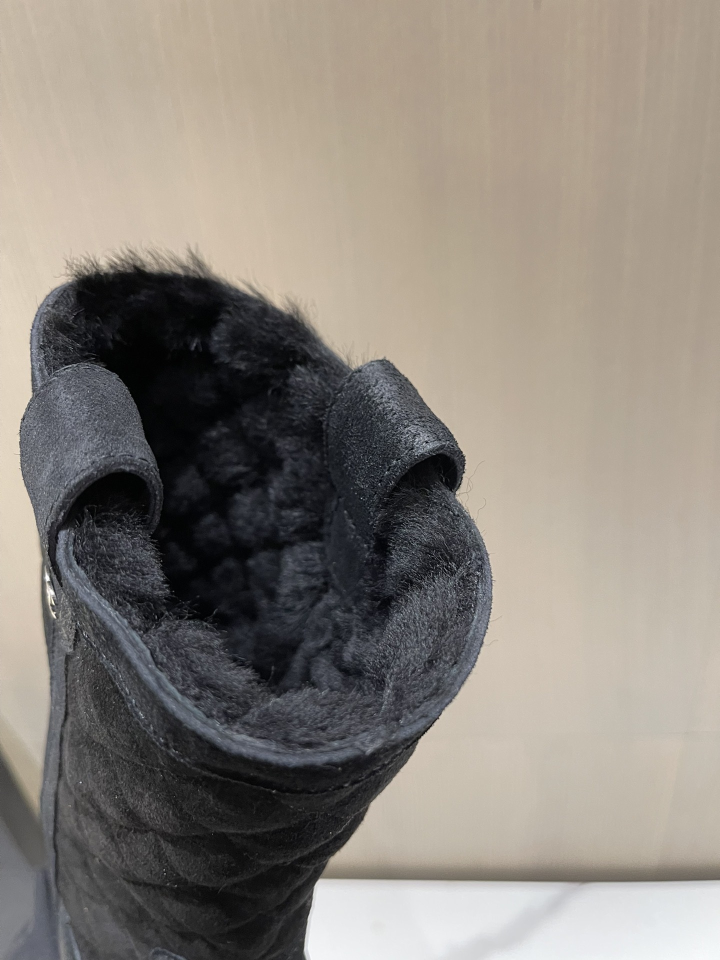 A pair of black Chanel quilted suede winter boots with fur lining and silver CC logo detail on a marble tabletop. - Hình 9