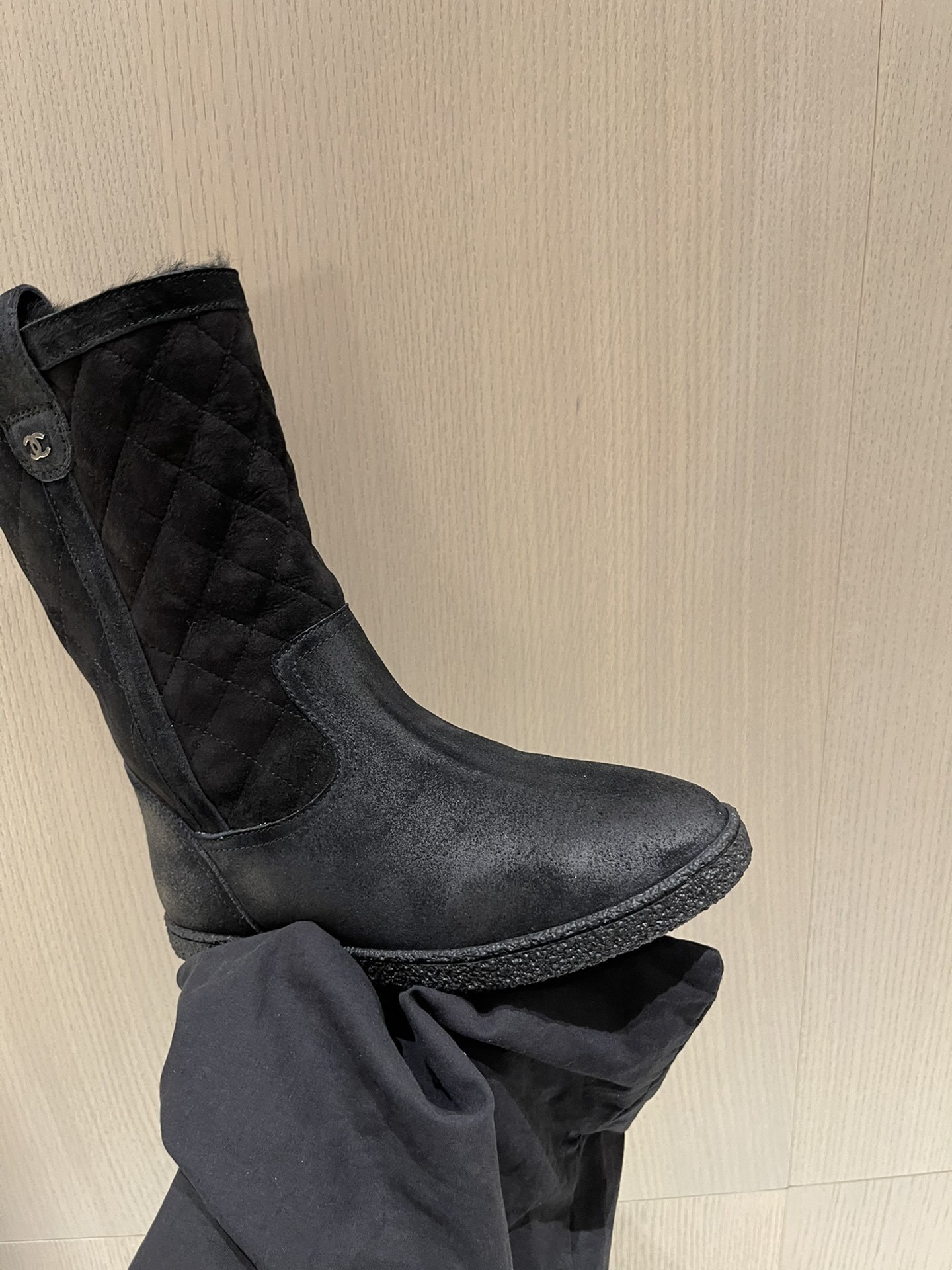 A pair of black Chanel quilted suede winter boots with fur lining and silver CC logo detail on a marble tabletop. - Hình 7