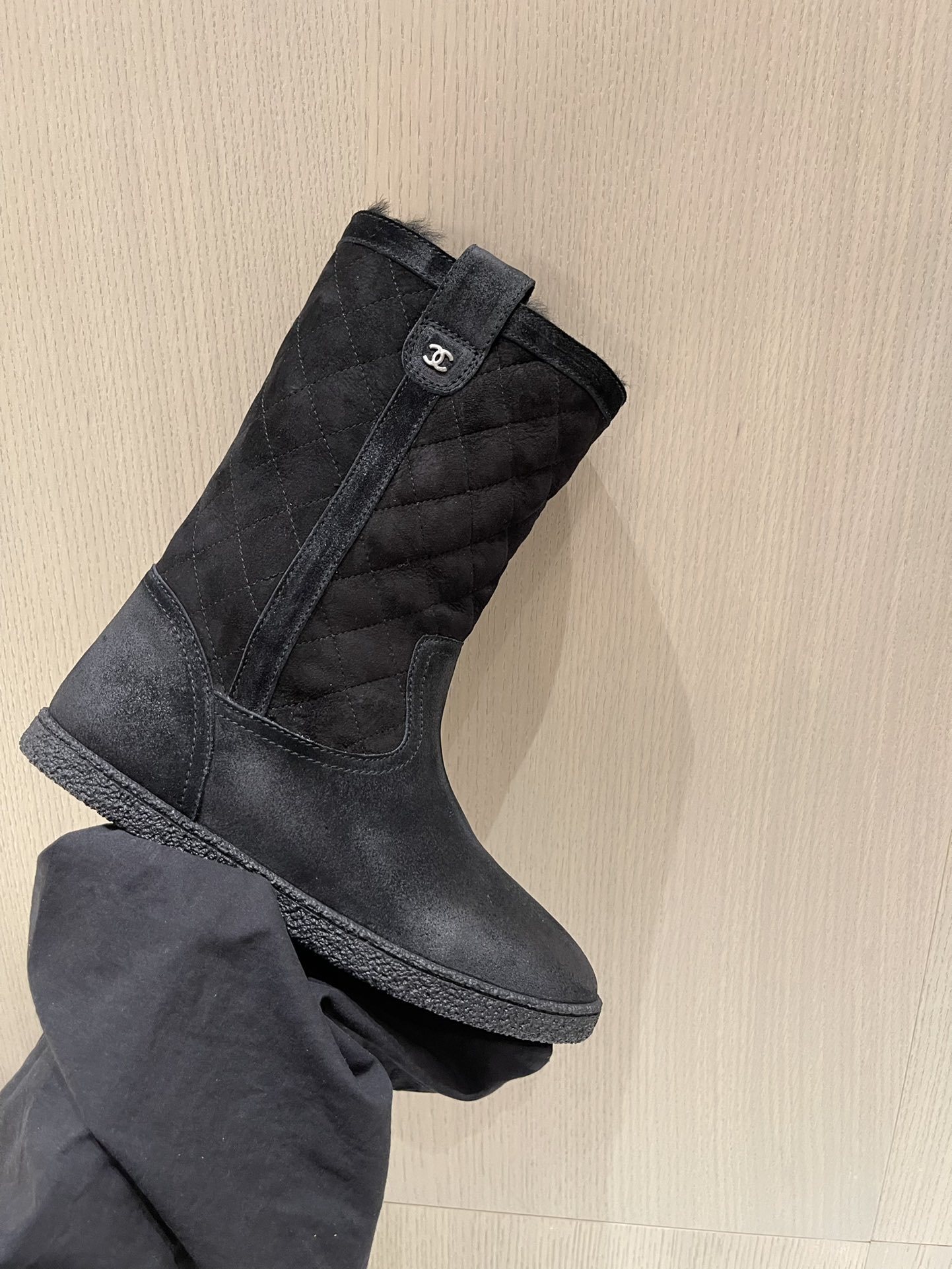 A pair of black Chanel quilted suede winter boots with fur lining and silver CC logo detail on a marble tabletop. - Hình 6